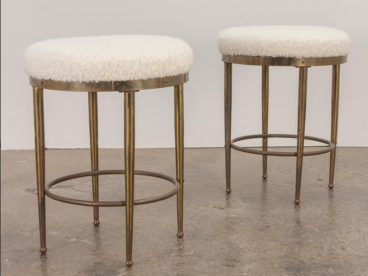 Vintage pair of low stools in the style of Mastercraft. Lovely patina to the elegant brass frames, supported by slender tapered legs and footrests. Topped with newly upholstered cushions in a luxurious ivory boucle that adds interesting texture to