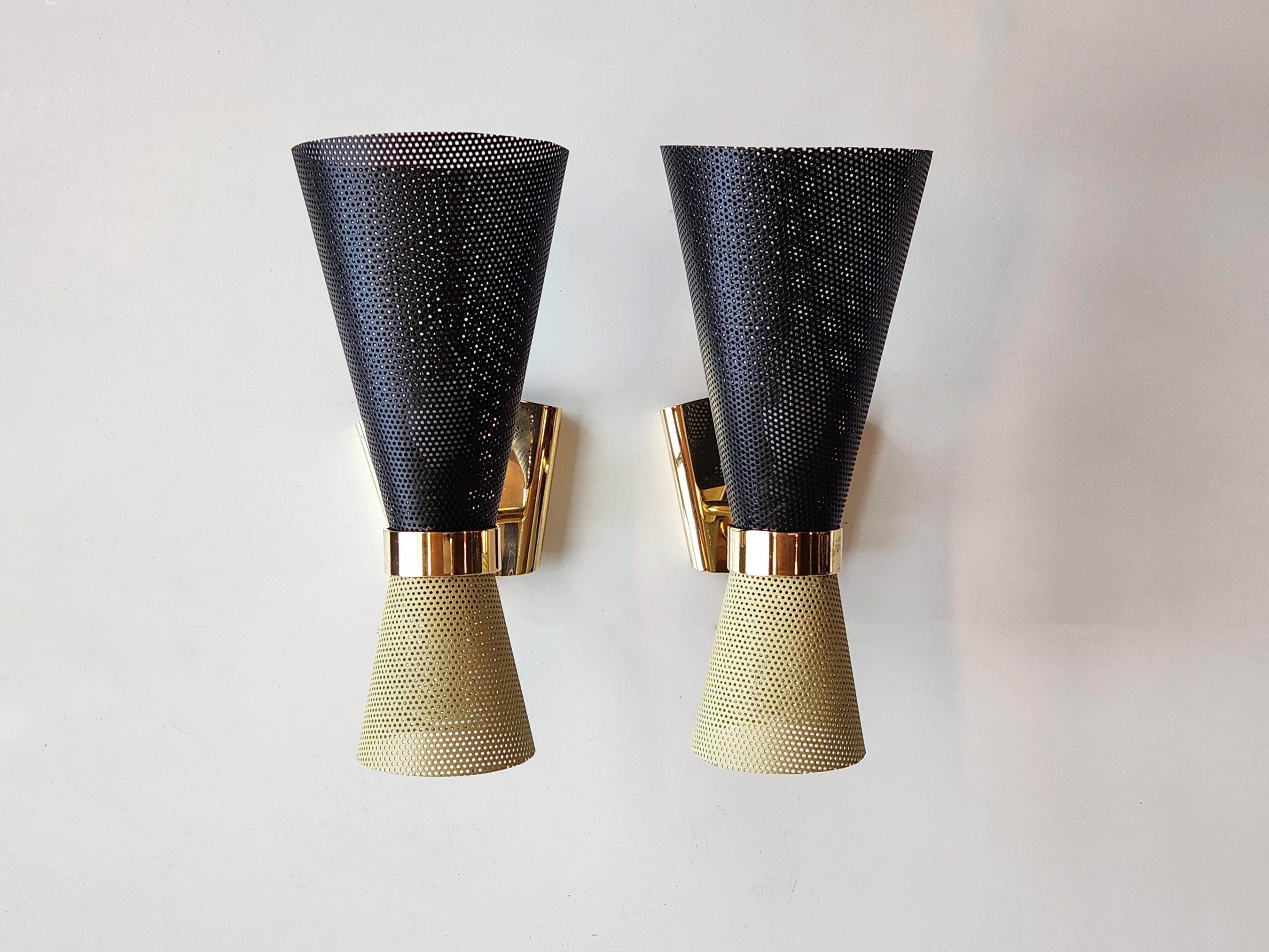 Very rare and exquisite sconces from the artist.

Two perforated metal shades joined together by a solid brass ring. The brass ring is fixed to the arm which connects the fixture to a brass canopy.