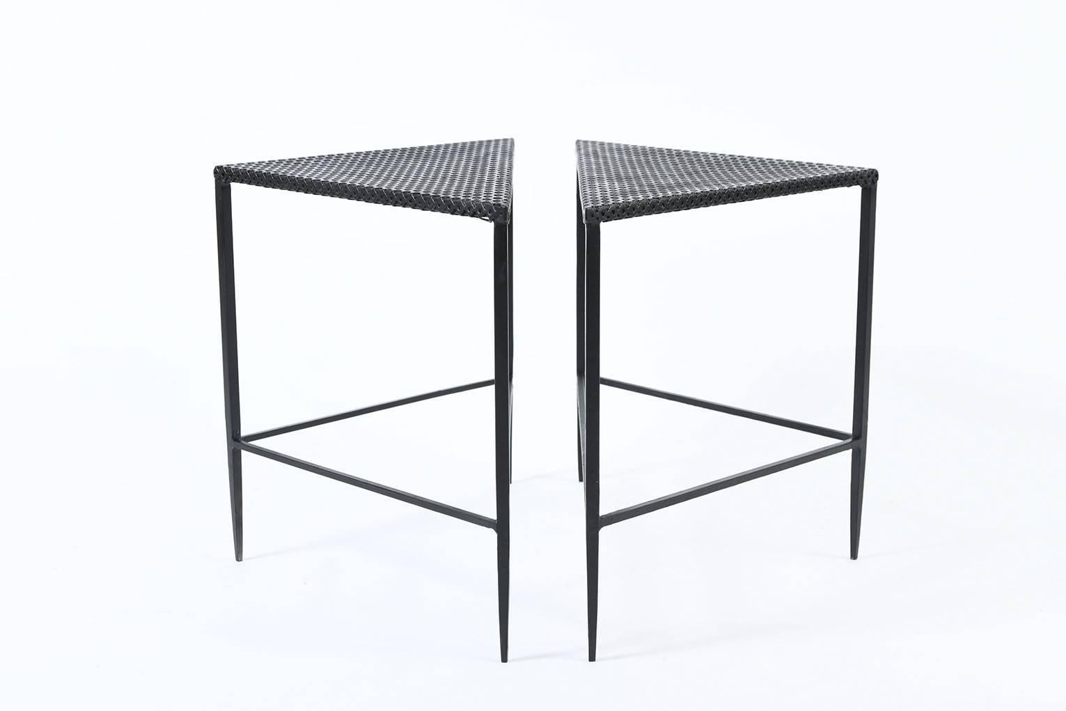 A pair of black enameled iron and rigitule two tiered triangular side tables, on tapered legs, in the manner of Mathieu Mategot (1910-2001)
France, circa 1955.