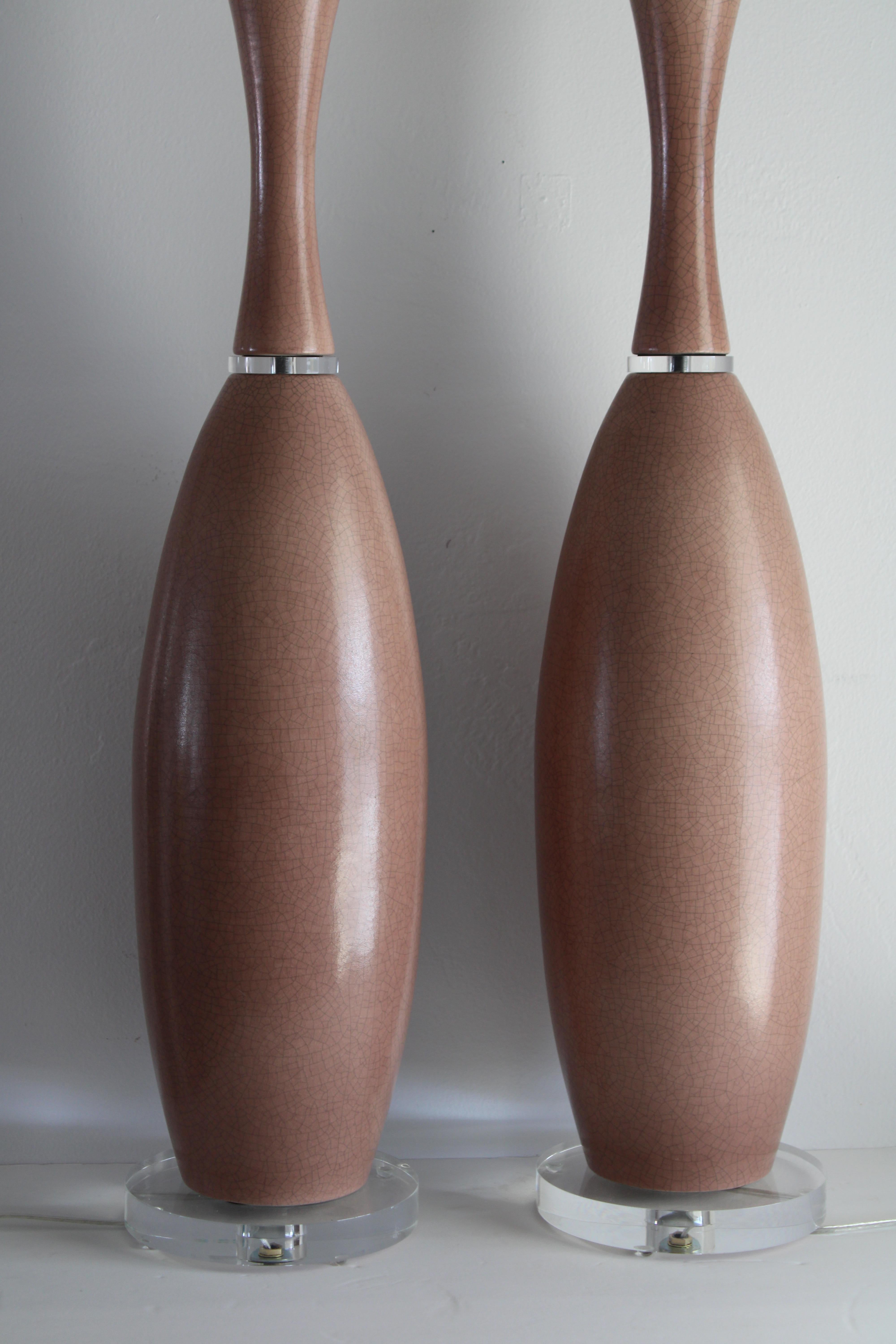 Pair of mauve ceramic lamps on lucite bases. We removed the brass base and mid section and replaced them with lucite. The top portion of the canopy where the brass neck is attached is still part of these lamps. Lamps have been professionally rewired