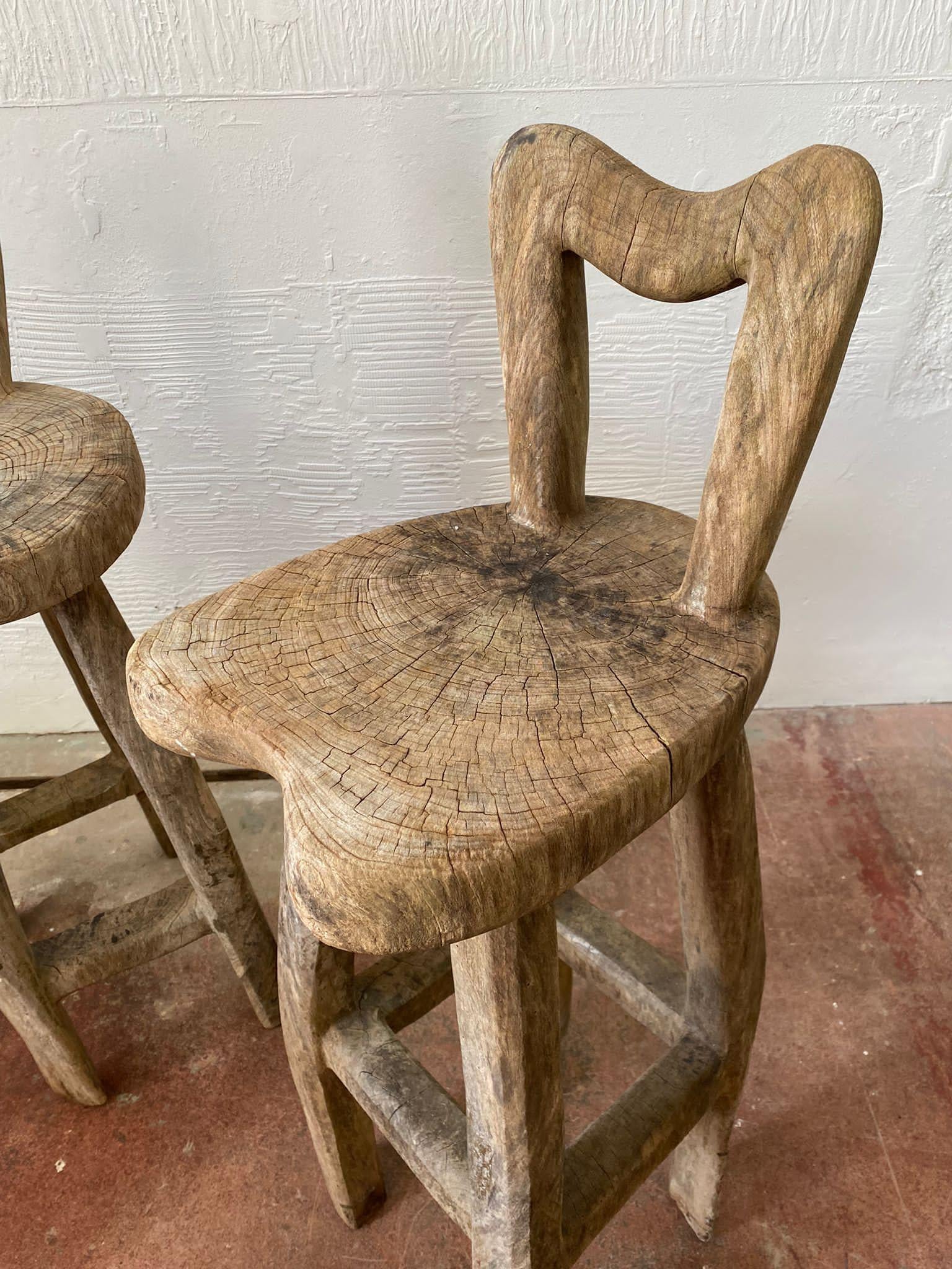 A pair of sculptural stools made by the artist Maxie Lane. Carved out of one piece of wood, they are unique and rustic.
The stools are tall perching seats. The raw and open wood finish are light, neutral and natural in appearance. They are wonky,