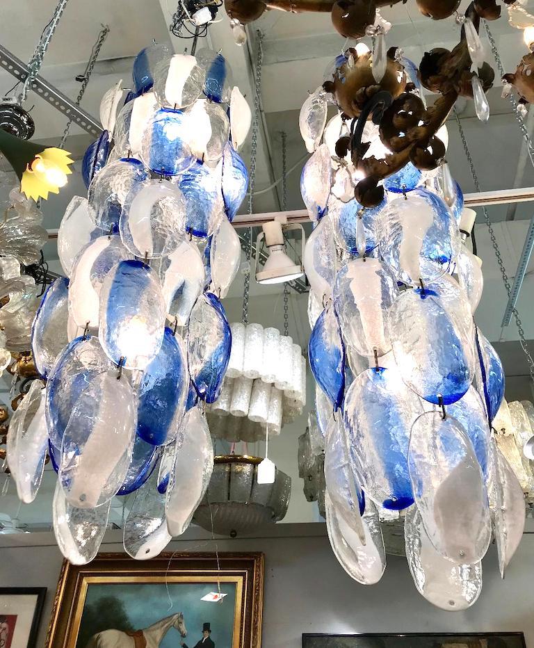 A stunning pair of glass disk chain chandeliers by the Italian lighting house Mazzega, circa 1970. Each chandelier is made of hand blown oval shape domed glass disks. The disks hang in chains of five pieces alternating clear with a white or clear
