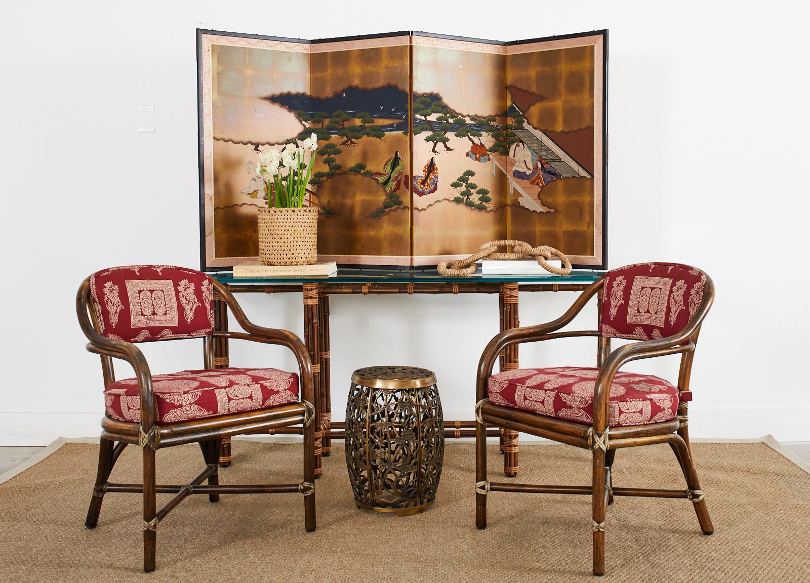 Organic modern pair of rattan armchairs by McGuire featuring an exotic Rajasthan style upholstery fabric with paisley floral motifs over a crimson ground. Crafted from bent rattan the sinuous frames have gracefully curved arms and a caned back. The