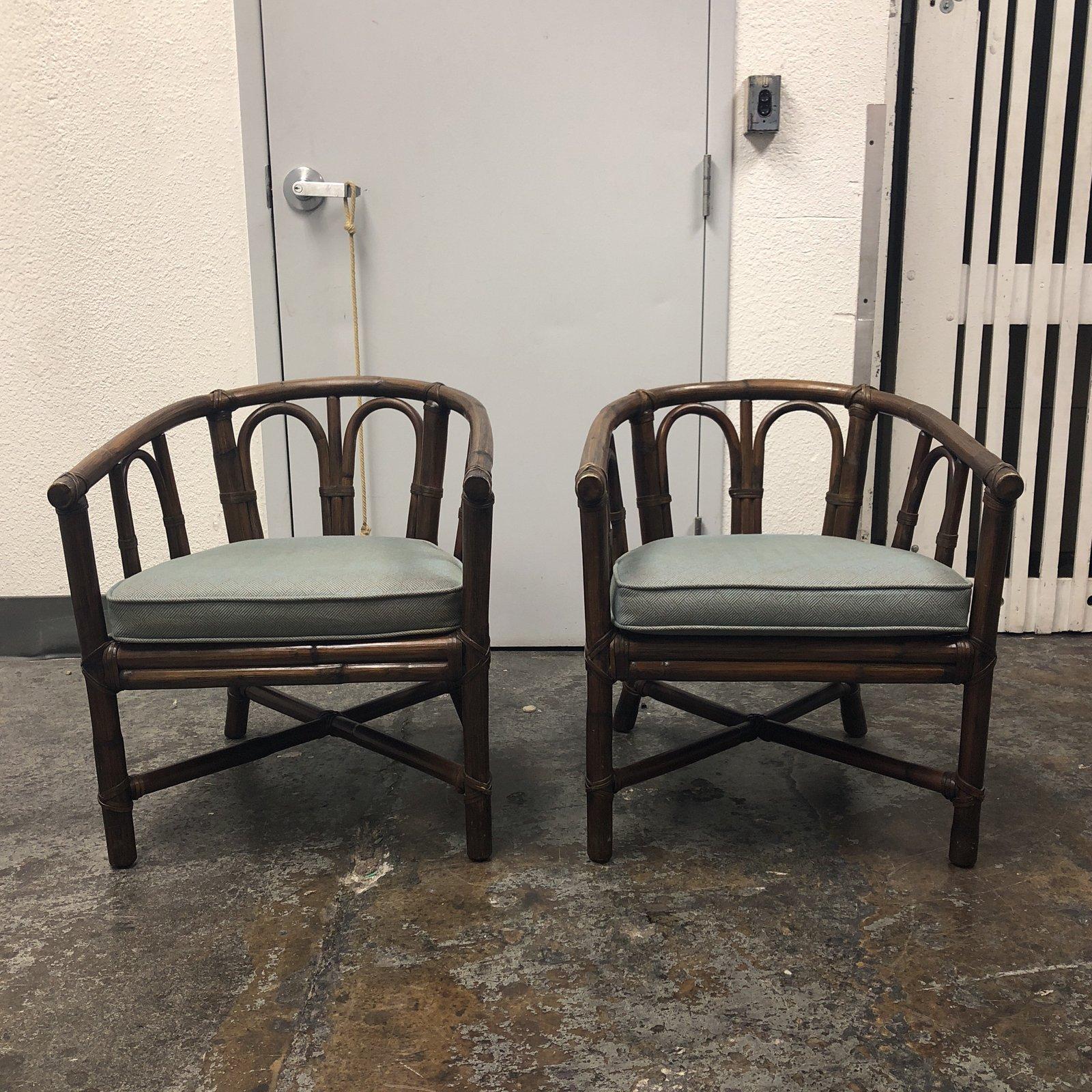 A pair of vintage bamboo barrel and cushion McGuire club chairs. The removable seat cushions are upholstered in a light faded teal fabric with a faint crosshatch pattern. The bent cane backings are reinforced with a generous application of wicker