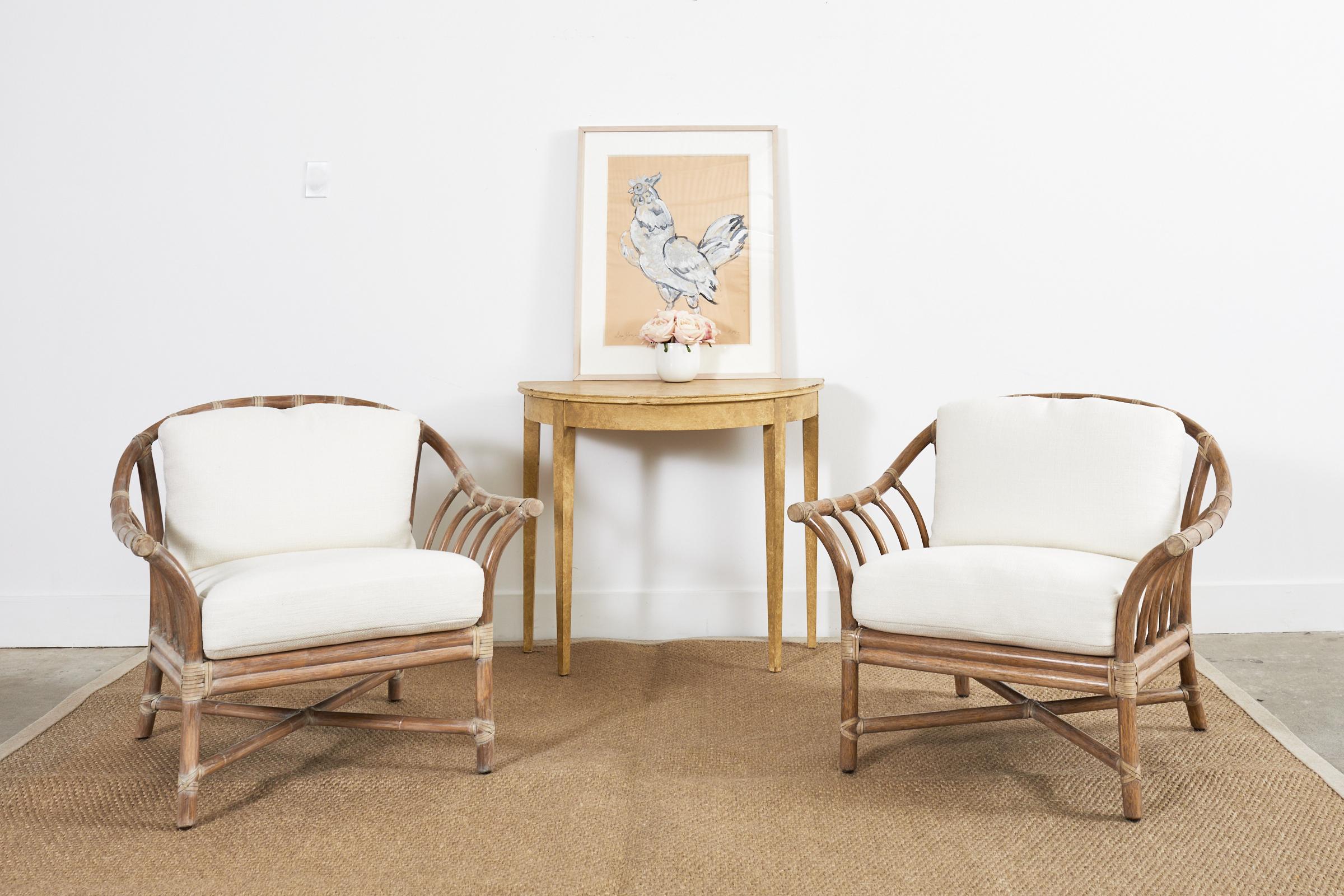 Gorgeous pair of oversized bent rattan lounge chairs and ottoman made in the California organic modern coastal style by McGuire. The chairs feature a large horseshoe shaped bent rattan frame with gracefully curved supports. The frame is reinforced