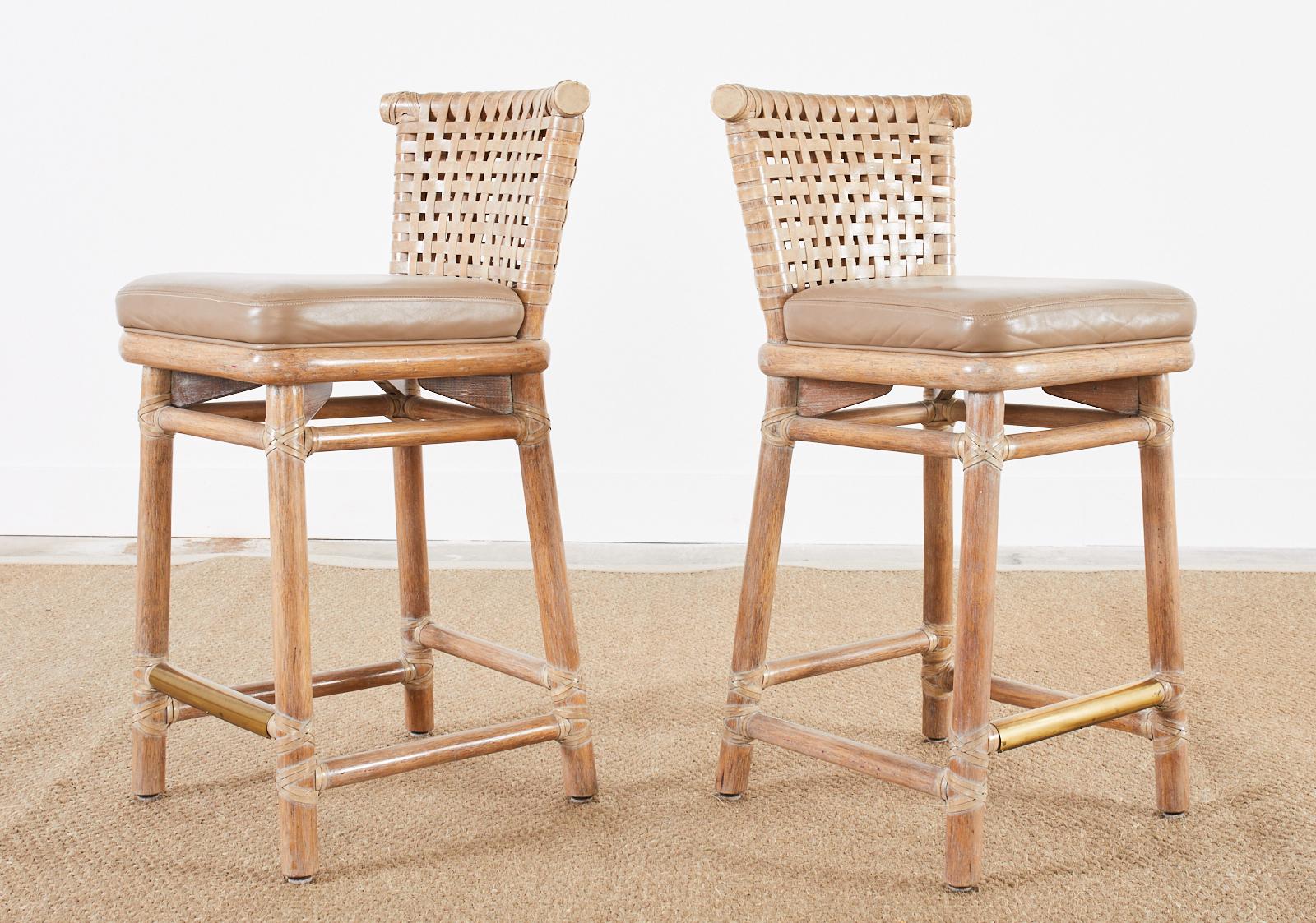 Gorgeous pair of organic modern rattan bar stools made by McGuire. The counter height stools feature a rattan and oak frame with a lightly cerused finish. The seats have a woven lattice leather rawhide back support with a thick curved rattan top