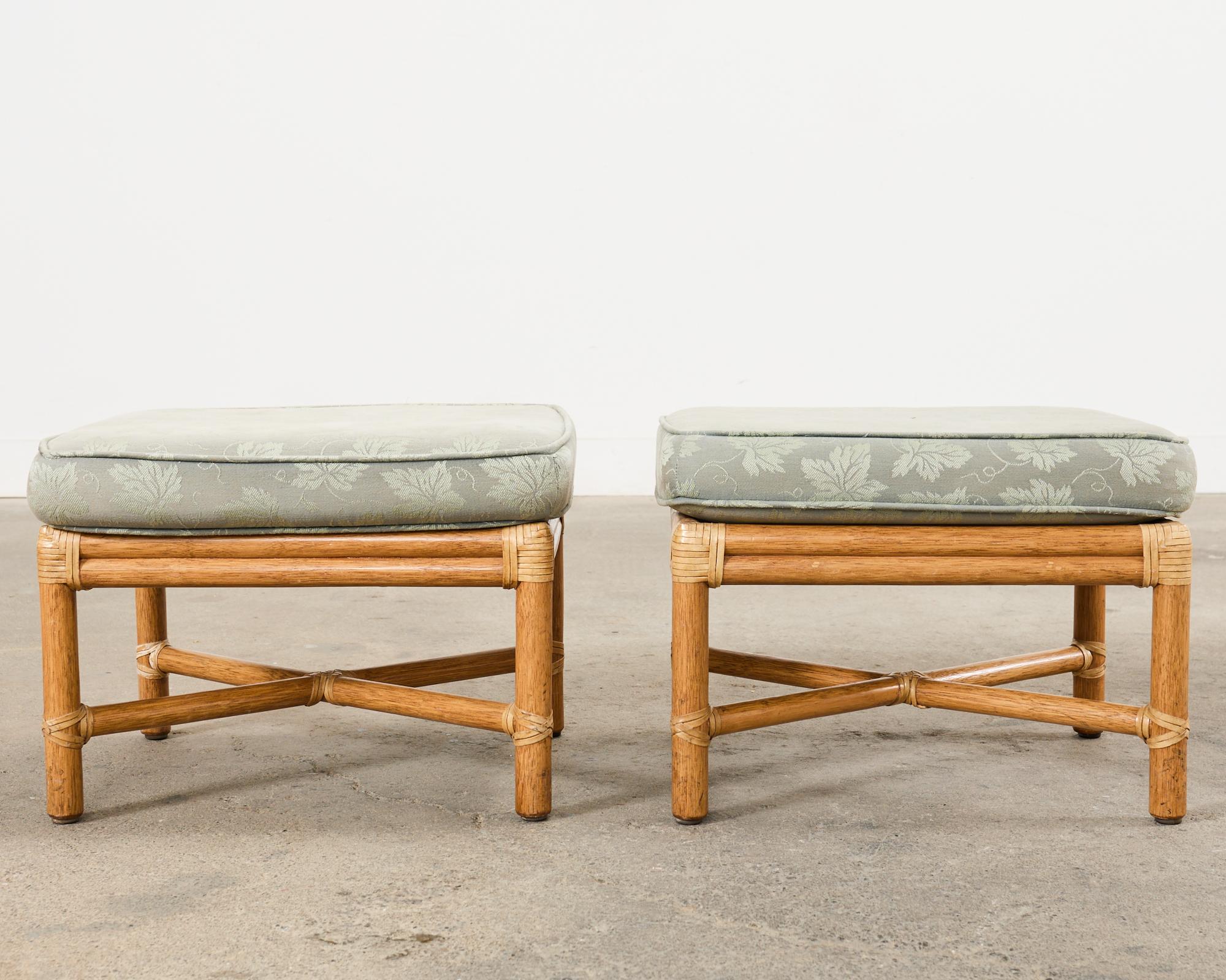Handsome matched pair of bamboo pole rattan footstools or ottomans made in the California coastal organic modern style by McGuire. The stools feature rattan poles lashed together with rawhide strapping in a complimentary cream toned leather. The