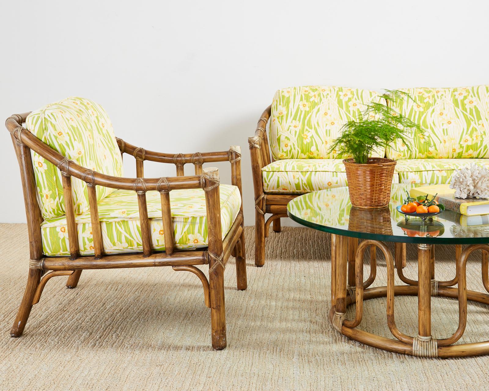Genuine McGuire pair of bamboo rattan lounge or club chairs made in the California organic modern style. The chairs feature thick rattan bent pole frames lashed together with leather rawhide laces. Topped with bright floral motif upholstered