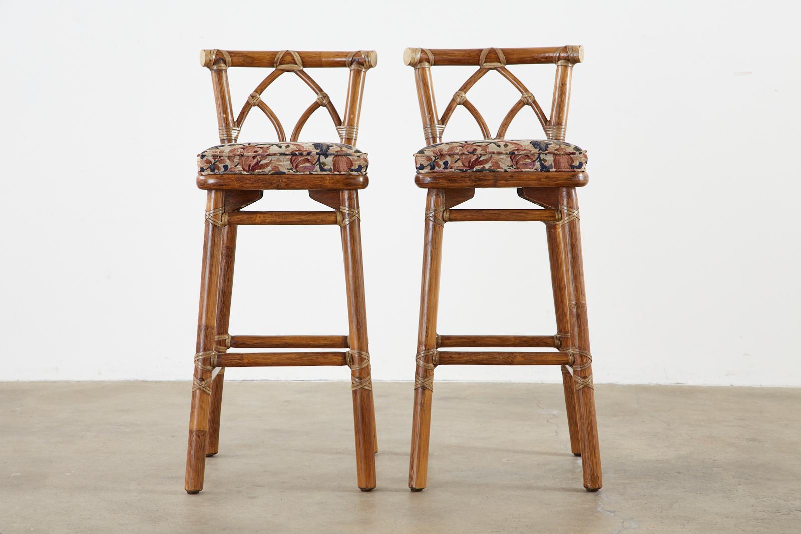Genuine pair of bamboo rattan bar stools made in the California organic modern style by McGuire, San Francisco. The chairs feature a thick rattan pole frame lashed together with leather rawhide laces. Decorated with an arch motif back splat and