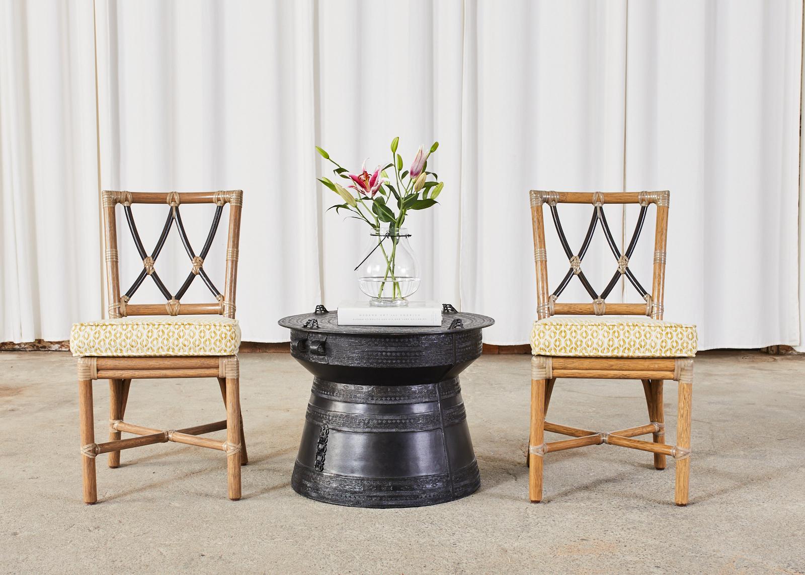 Organic modern pair of rattan dining chairs made by McGuire known as Pixley chairs model #MCJSC17. The chairs feature a narrow frame crafted from thick rattan poles. The square back splat is decorated with a pair of x-motifs in ebonized finishes.