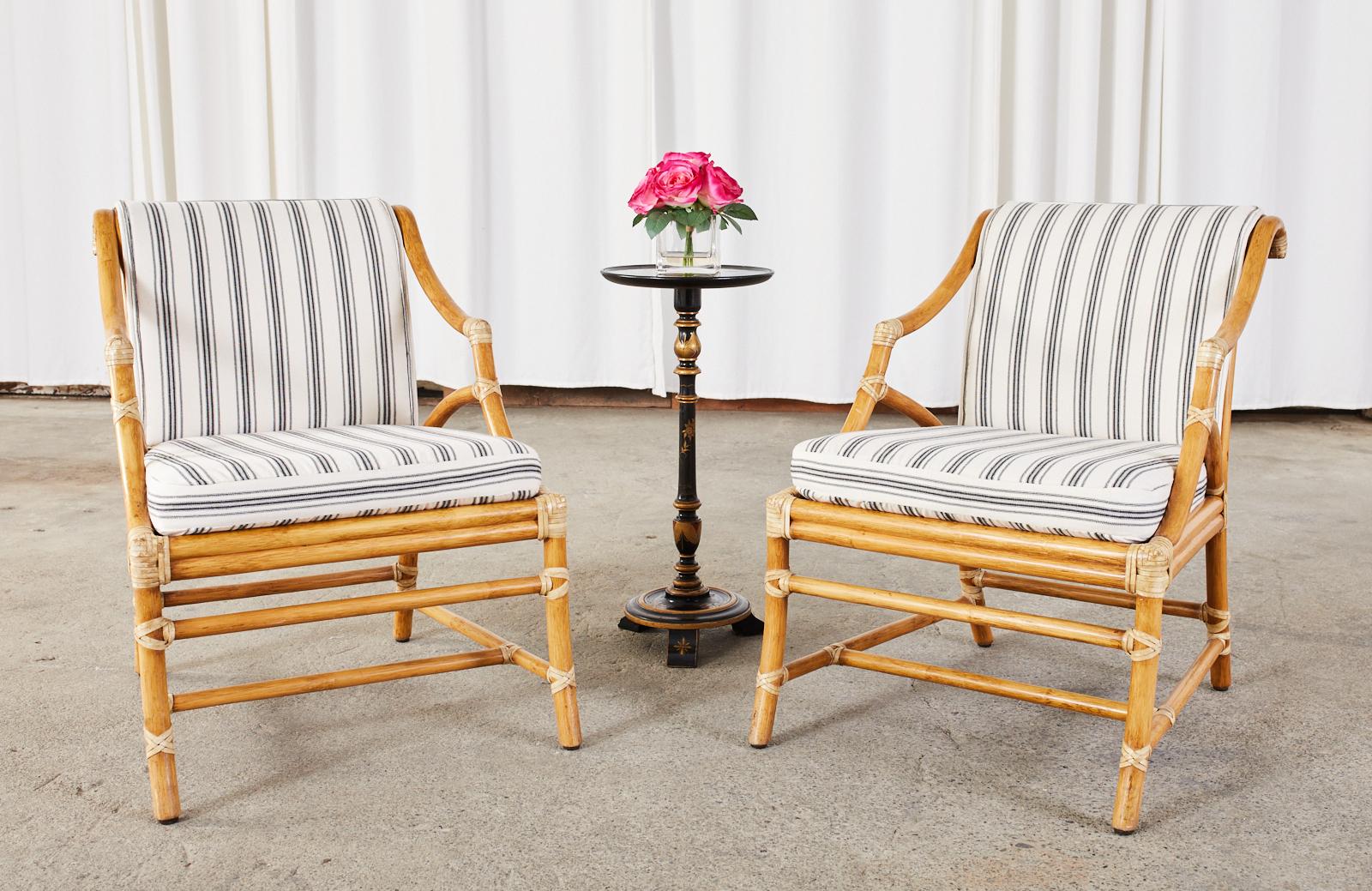 Stylish pair of genuine McGuire lounge chairs or club chairs featuring a caned seat and back designed by Elinor McGuire with gracefully curved, and bent rattan reinforced with light colored leather rawhide laces. Topped with new striped cream and