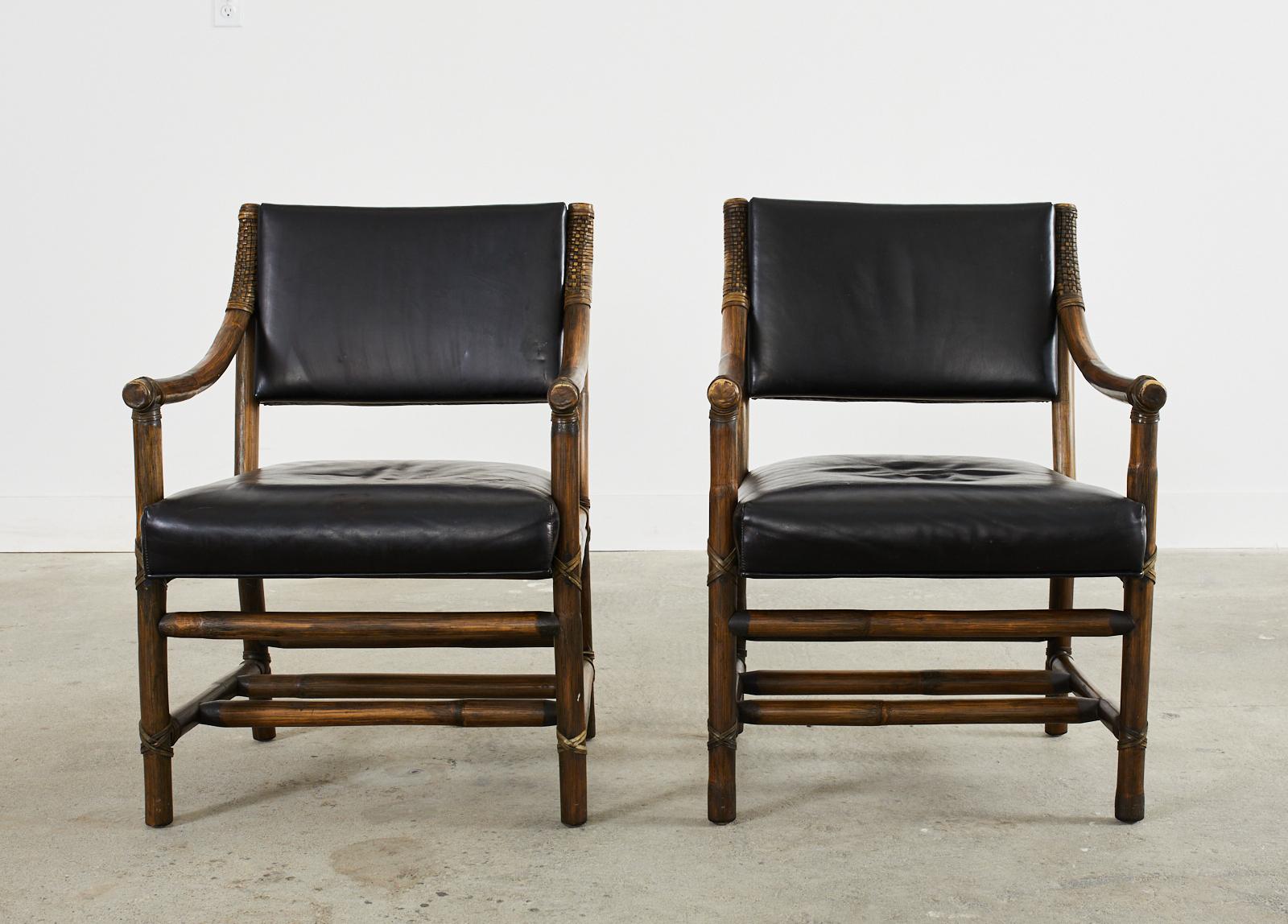 Mid-century organic modern pair of library armchairs or dining chairs made by McGuire. The chairs feature a rattan pole frame lashed together with leather rawhide laces. The chairs have gracefully curved arms and thick black leather covered seats.
