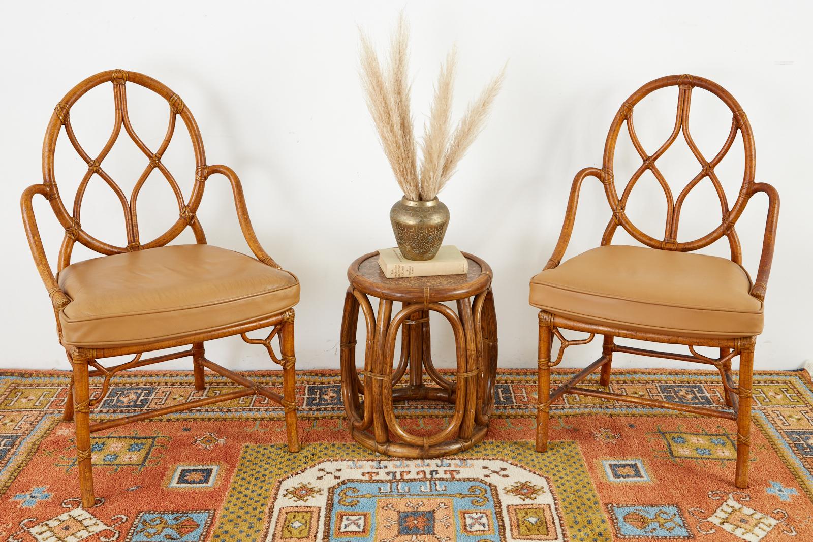 Handsome pair of bamboo rattan dining chairs made in the California organic modern style by McGuire San Francisco. The chairs have a round back with gracefully curved arms conjoined to a cane seat topped with a thick leather seat cushion. The chairs