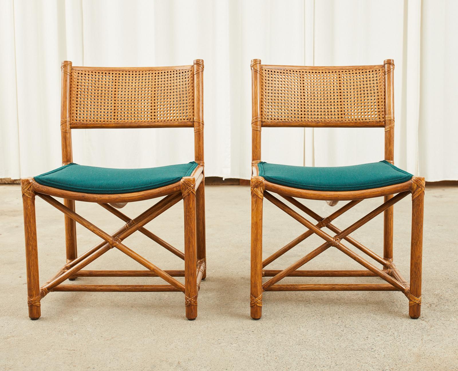 Genuine and rare pair of rattan framed dining chairs made in the California organic modern style by McGuire. The chairs feature a double caned back and leather rawhide laces on the exposed joints. Upholstered with a rich emerald green fabric on the
