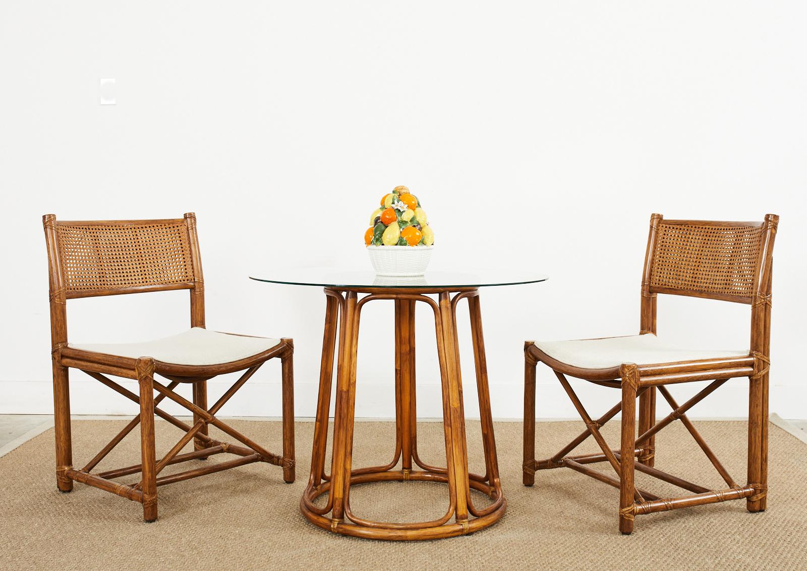 Genuine and rare pair of rattan framed dining chairs made in the California organic modern style by McGuire. The chairs feature a double caned back and leather rawhide laces on the exposed joints. Newly upholstered with a rich cream and white fabric