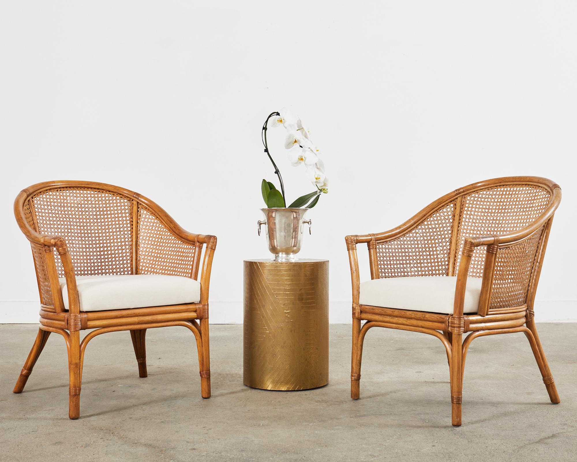Mid-century modern pair of rattan barrel back armchairs made in the organic modern manner and style of McGuire. The chairs feature a horseshoe shaped crest inset with woven cane on the back and sides. The seats have a thick cushion measuring 24