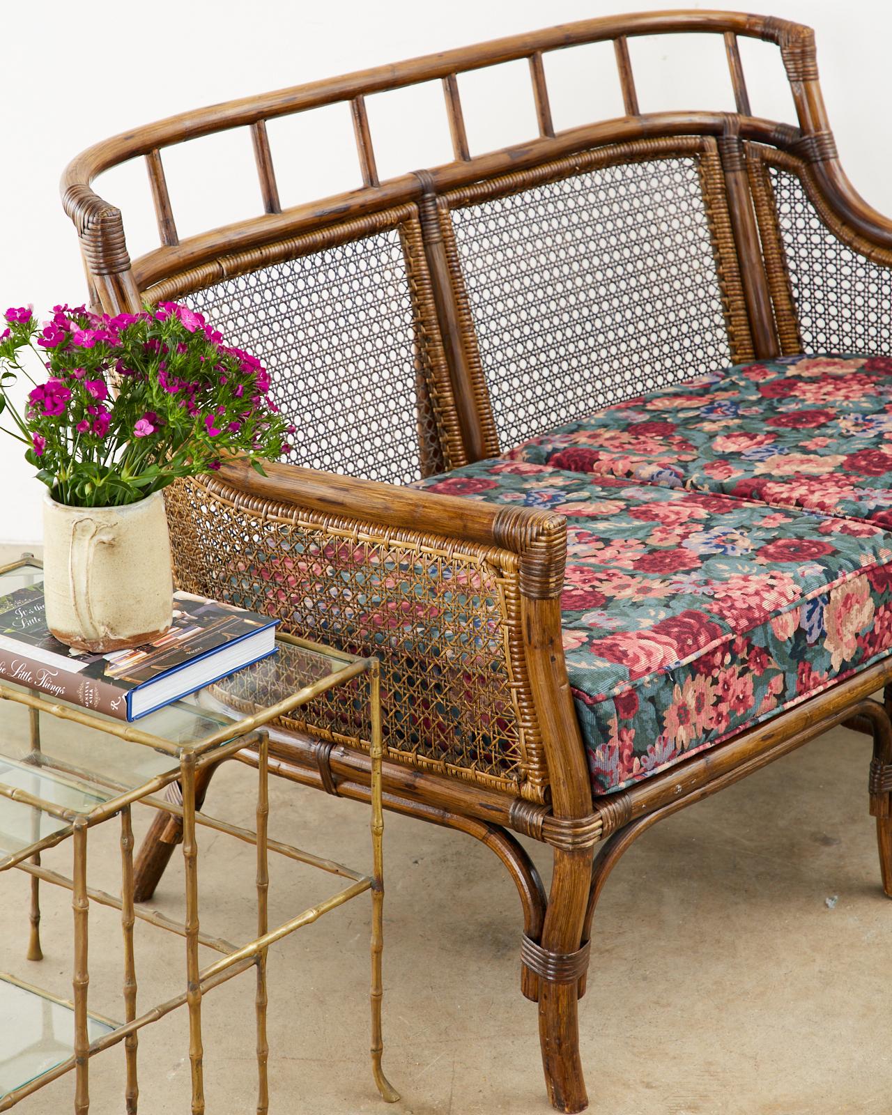 Handsome matched pair of bamboo rattan frame settees or loveseats made in the organic modern style and manner of McGuire. The pair feature curved back rattan frames inset with cane and lashed together with wicker strapping. Topped with thick