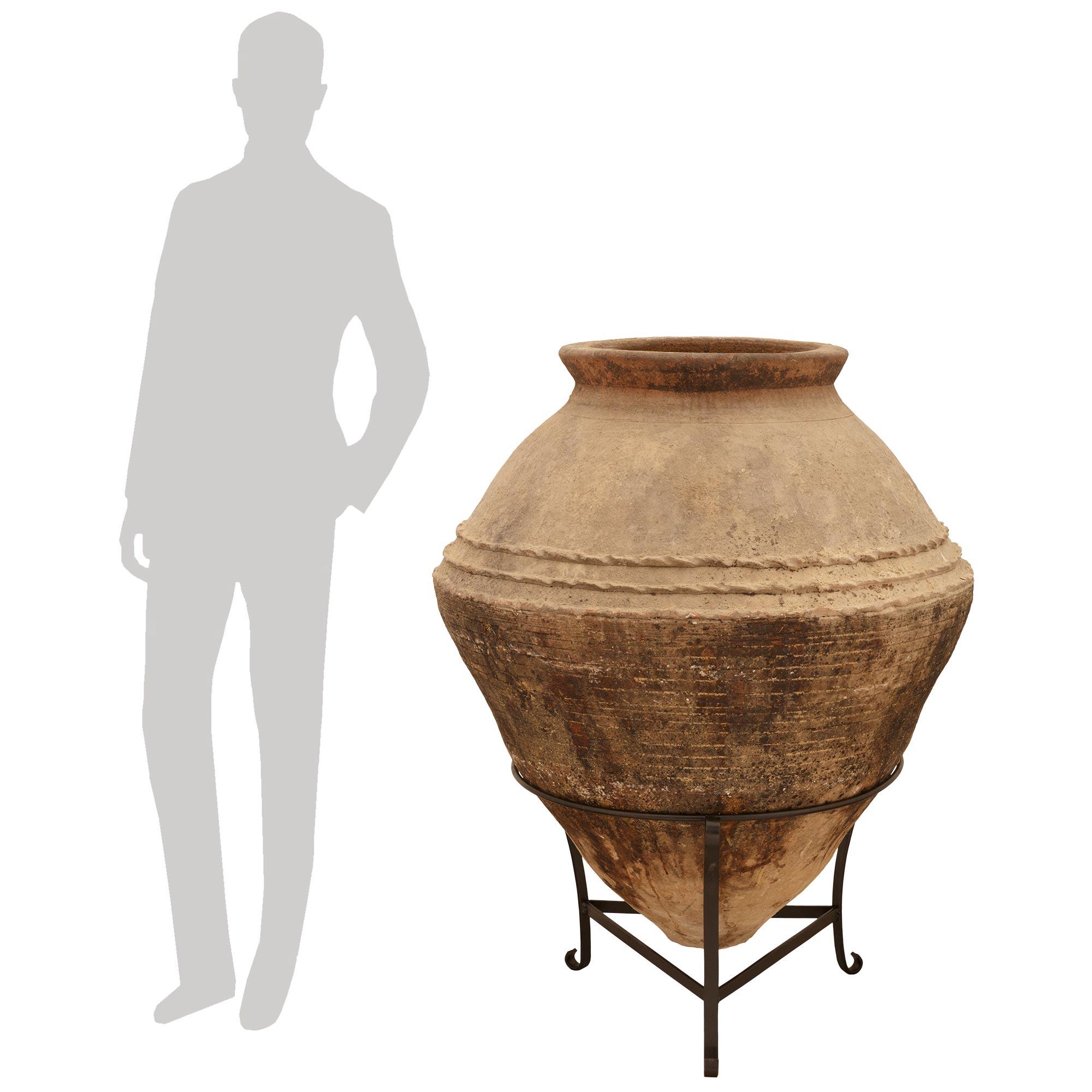 Impresionante pareja a gran escala de tinajas de olivas de terracota patinada mediterráneas del siglo XIX. Cada tarro de aceitunas, bello y extremadamente decorativo, se eleva sobre una base trípode de hierro forjado, y muestra una forma cónica