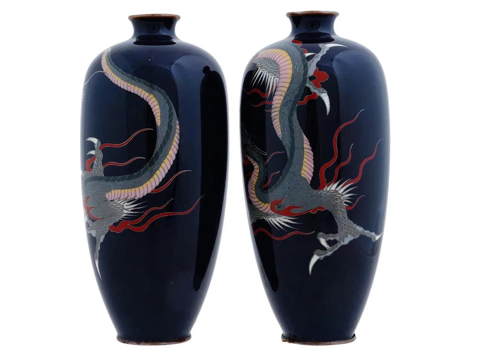 Un par de jarrones japoneses de alambre de plata esmaltado. Los jarrones tienen el cuerpo en forma de urna y el cuello estriado. Cada vajilla está esmaltada con una imagen polícroma de dragones sobre fondo azul oscuro realizada con la técnica