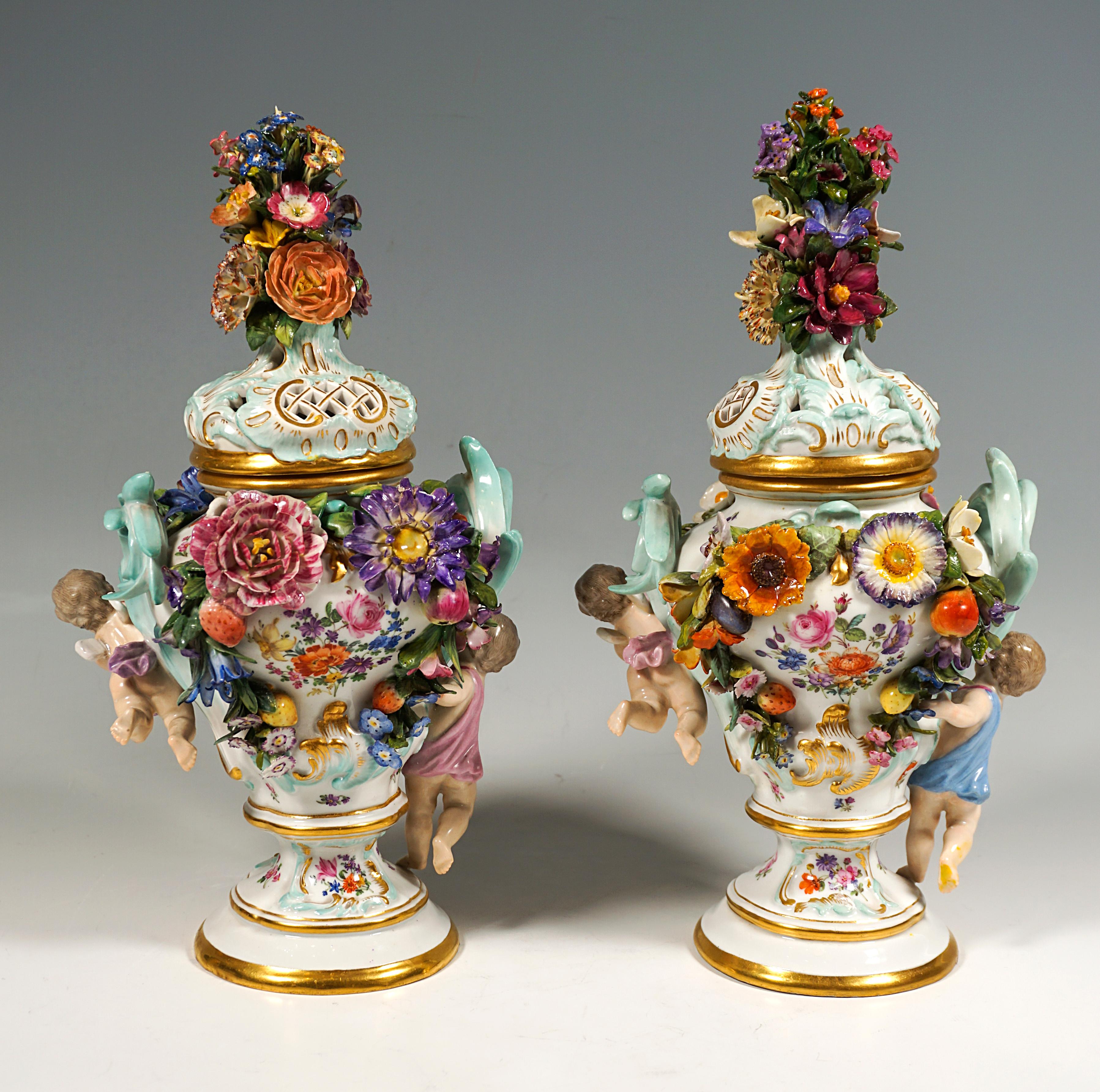Baluster-shaped vase body on a stepped, round base with a pierced lid, lavishly decorated with sculpted and colourfully painted flowers, leaves, fruit and rocailles, as well as two cupids on the sides, with coloured scattered flower decoration in