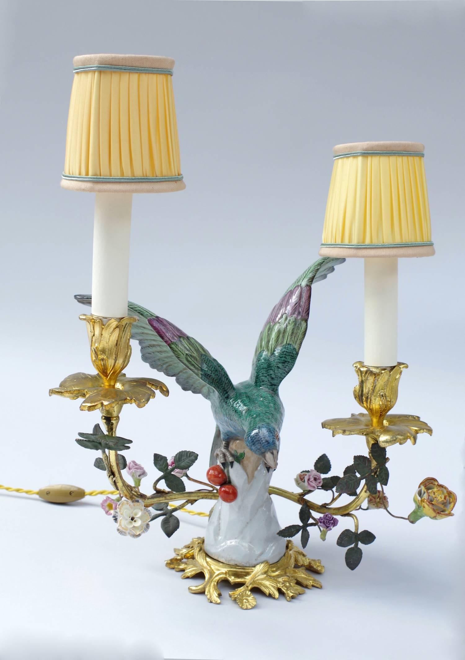Pair of two lights porcelain lamps, representing two budgies with deployed wings and perched on a naturalistic base. Retour ligne automatique
Rocaille style chiseled and gilt bronze mount. The two birds are framed with floral decoration on the bras