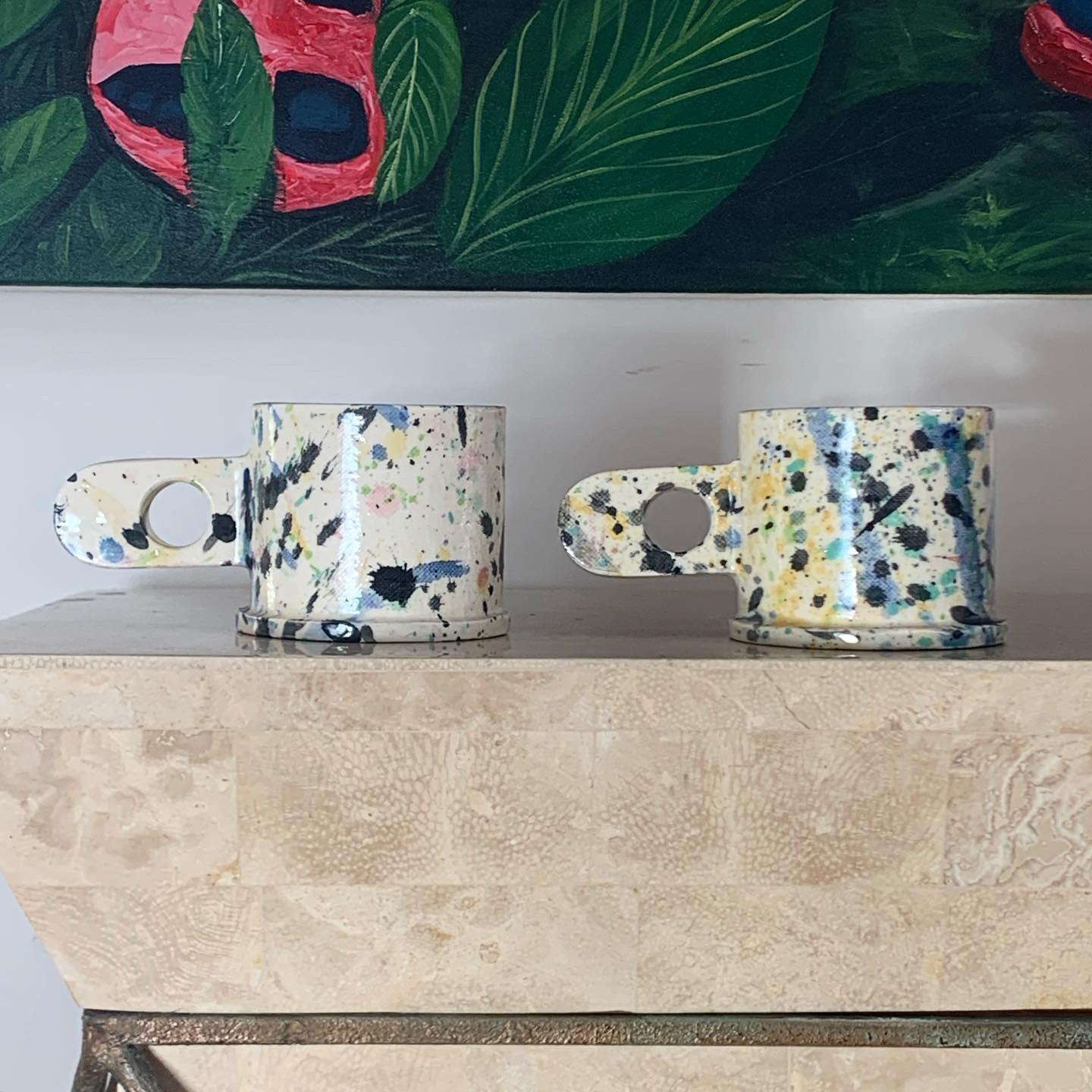 2 ceramic handmade mugs with multicolored paint splatter by veteran Memphis artist Peter Shire. These are hand painted so no two are the same. Limited edition. Each mug reads EXP 2012 in stamped relief text at the base. Immaculate condition.