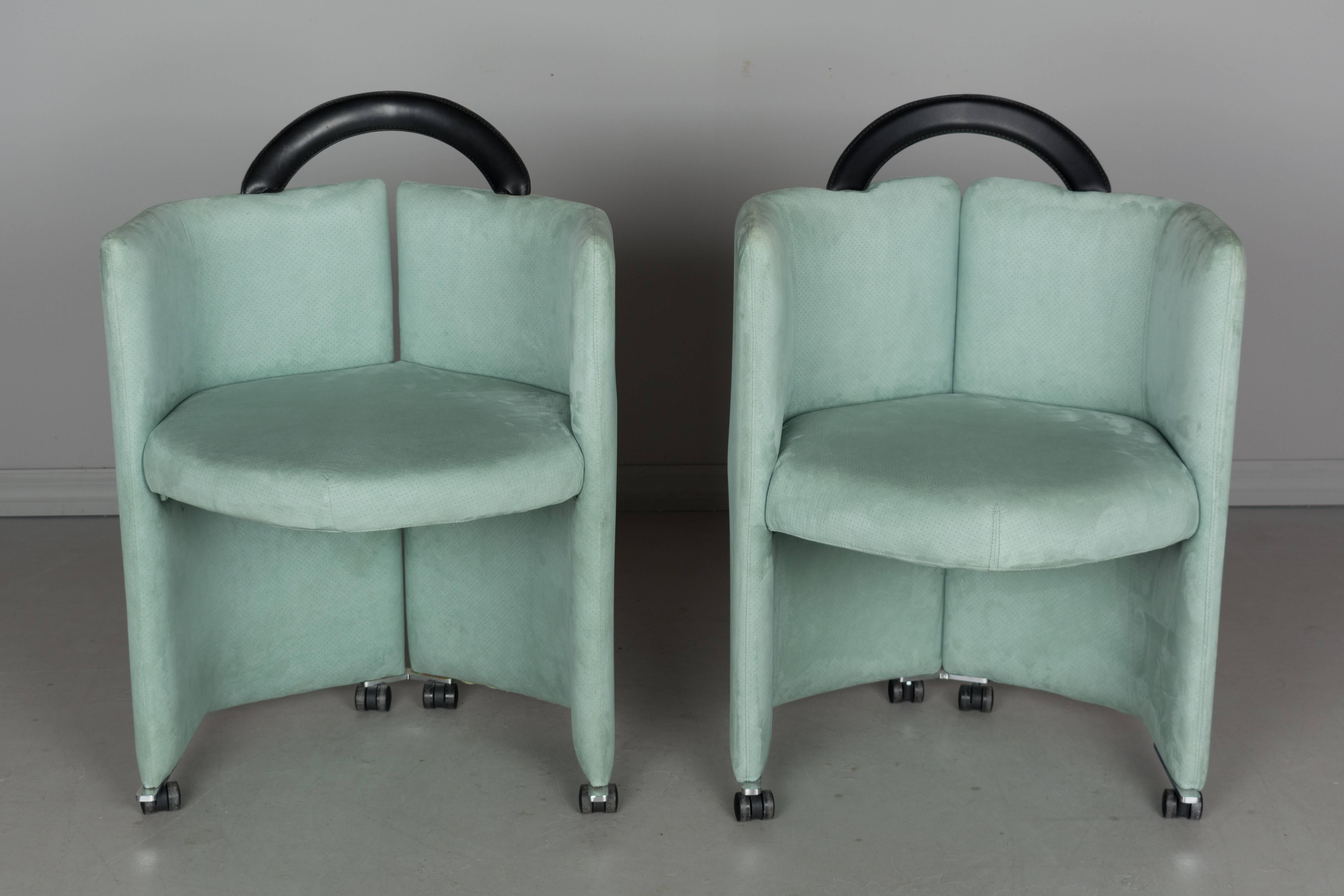 A pair of Italian Memphis style club chairs upholstered in a beautiful aqua color perforated ultrasuede fabric with black leather handle. These are stylish and comfortable chairs that glide easily on castors. Arm height 30