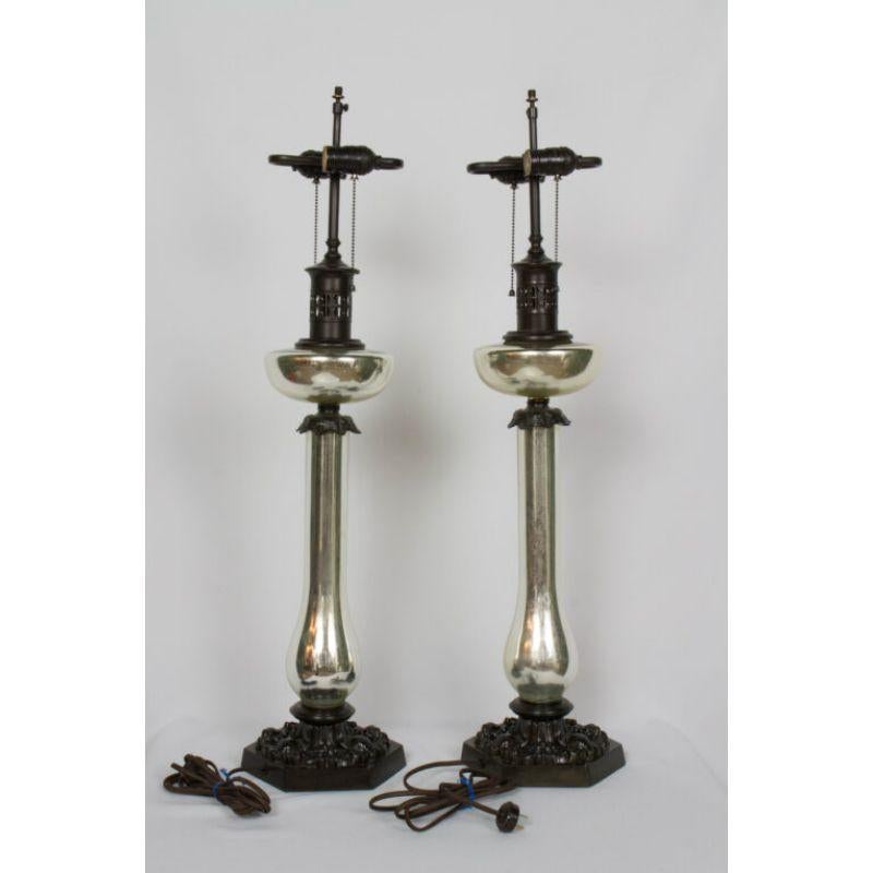 Pair of Mercury glass Banquet lamps. Made in the style of antique oil burning table lamps. Cast metal bases with Neo-rococo design, in a dark almost black patina. Tall slender mercury glass stem and mercury glass faux oil reserve. Faux burner and
