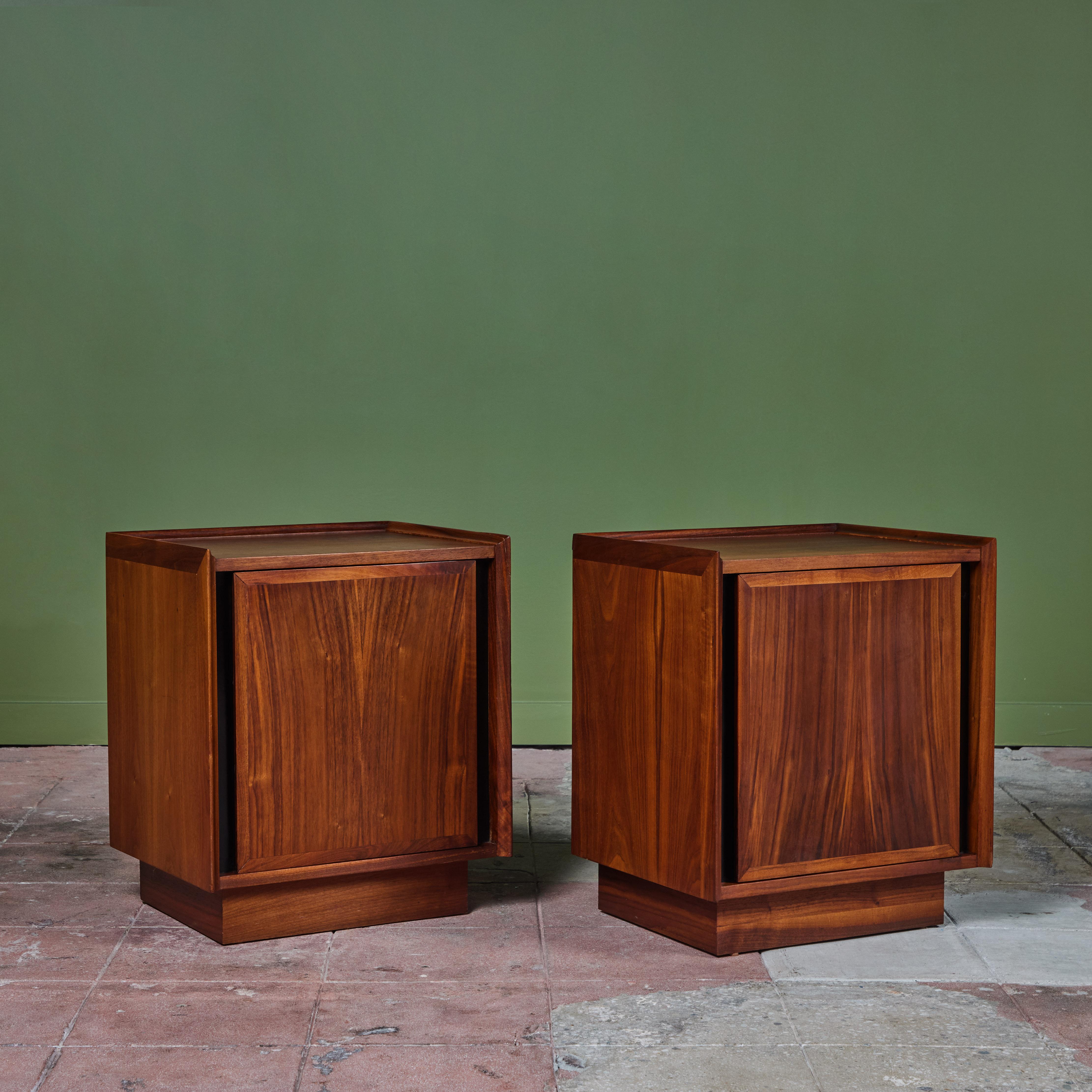 Pair of walnut nightstands by Merton L. Gershun for Dillingham, c.1960s, USA. The nightstands each feature a single door front with beveled sides. The hinged doors open to reveal a wide storage cabinet with pull-out white laminated drawers. The