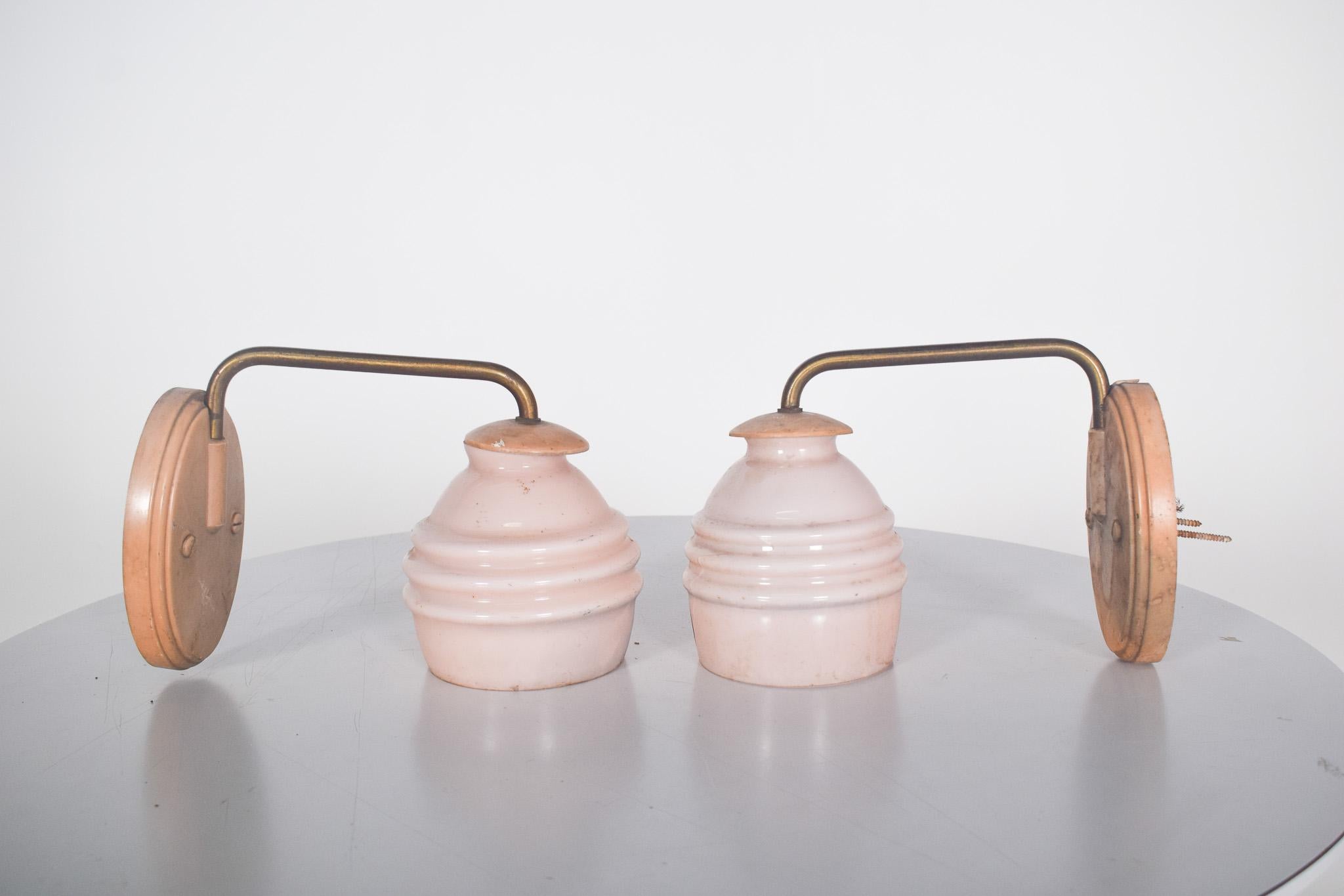 Pair of metal and pink glass wall lights. This elegant pair of wall lights features a metal structure in an aged gold tone and pink opaline glass shades. The classic and delicate design of these appliques adds a vintage charm to the piece,