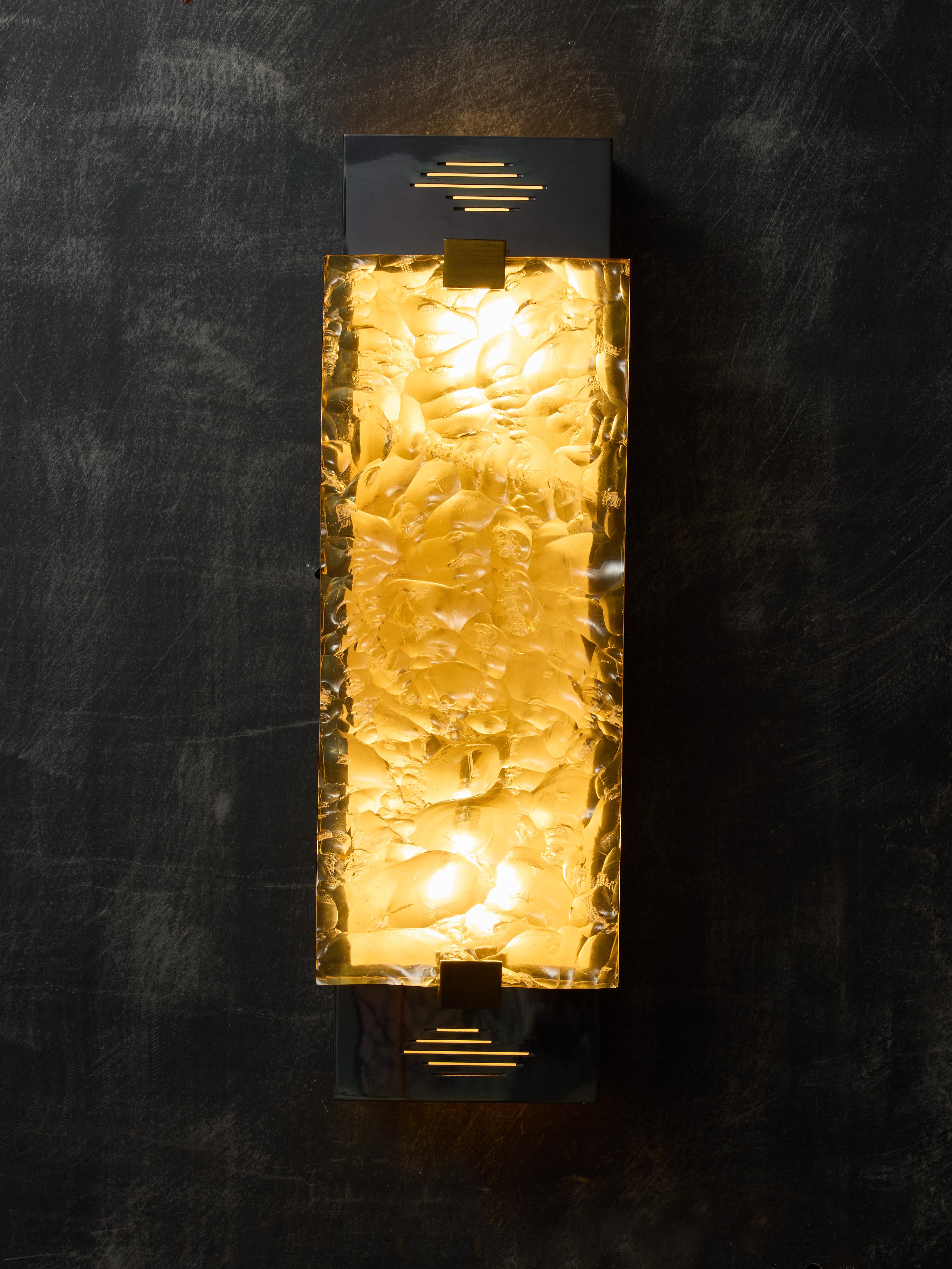 Pair of decorative wall sconces, made of a rectangular shiny metal box holding two lights with horizontal slits, covered with a slab of yellowed and hammered resin, hold by brass settings.

SERGE MOUILLE (1922-1988)

Serge Mouille is one of the most
