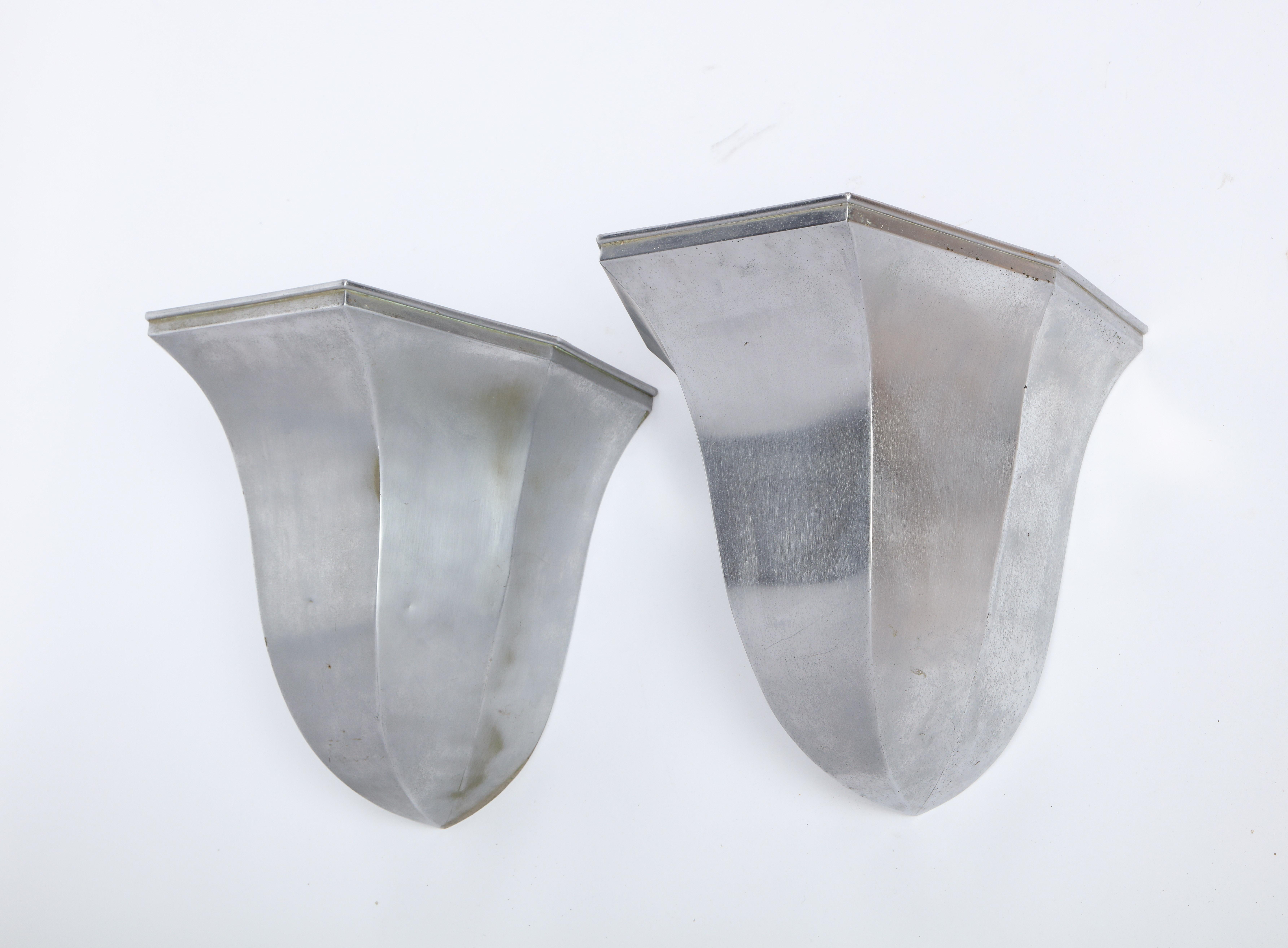 A pair of modern silver-tone metal tulip-form wall uplights. Characterized by its smooth reflective surface and sculptural flared rim, the light bears a label 'Birchall' to the interior. 

Property from esteemed interior designer Juan Montoya. Juan