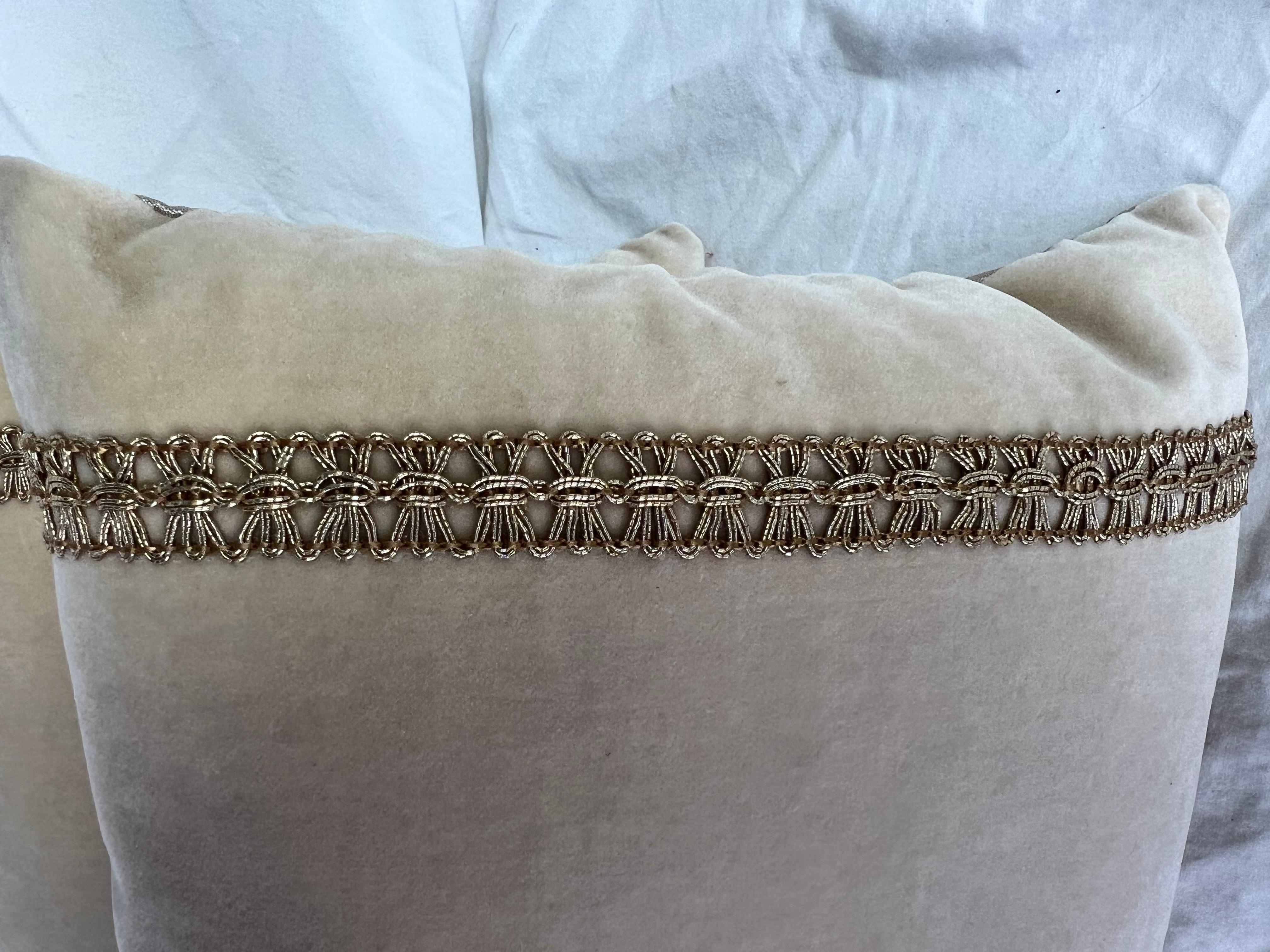 A pair of decorative pillows that have a minimalist and elegant design.  The pillows are cream colored silk velvet with silk backs.  Each pillow features a central embroidered design in gold, depicting a simple, stylized floral/leaf motif.  On both