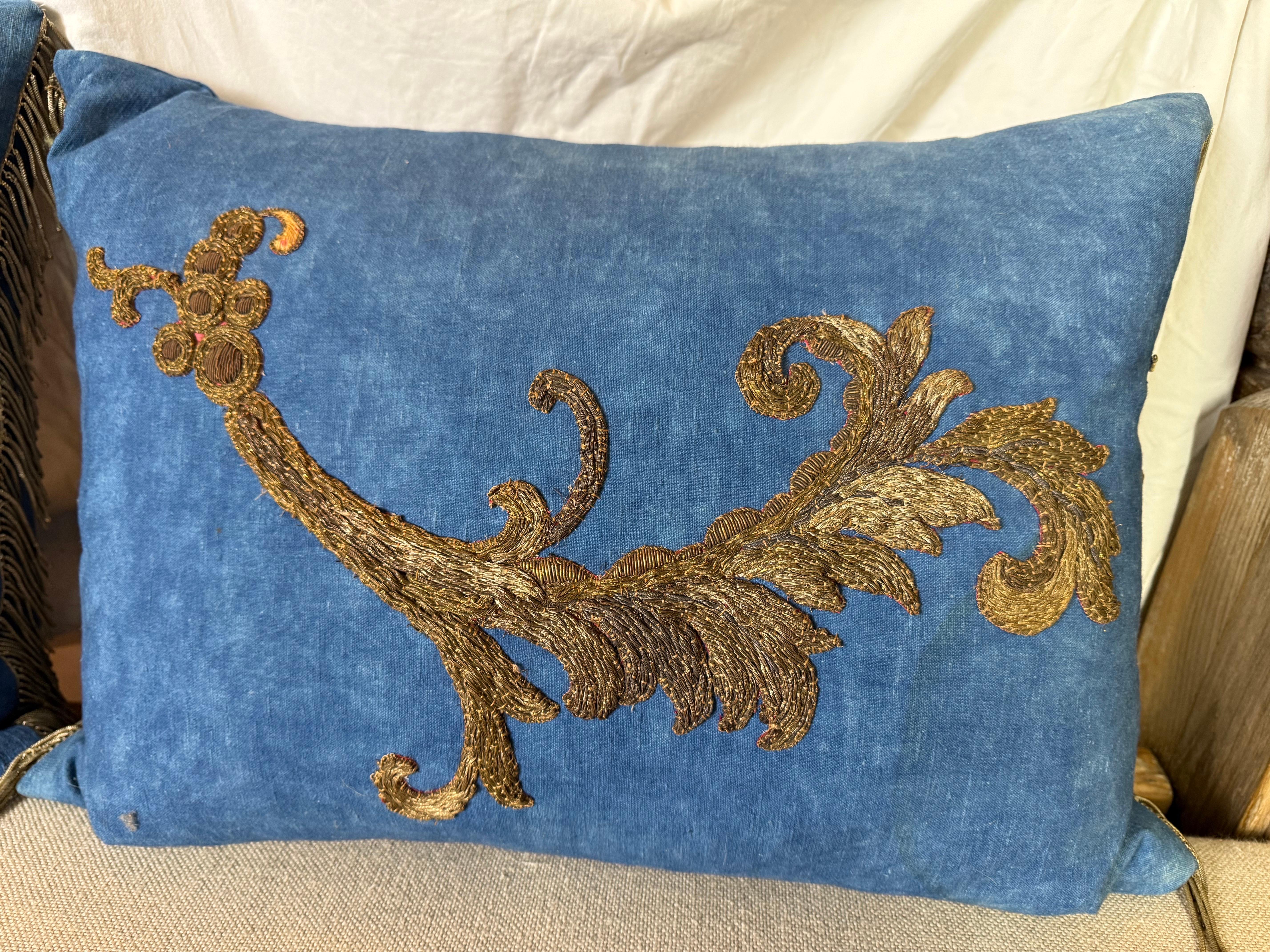 Coppia di eleganti cuscini in tessuto di lino vintage dal colore blu intenso. I cuscini sono caratterizzati da un intricato ricamo in oro con un disegno a foglie d'acanto, che ricorda le arti decorative europee classiche. Il ricamo metallico del XIX