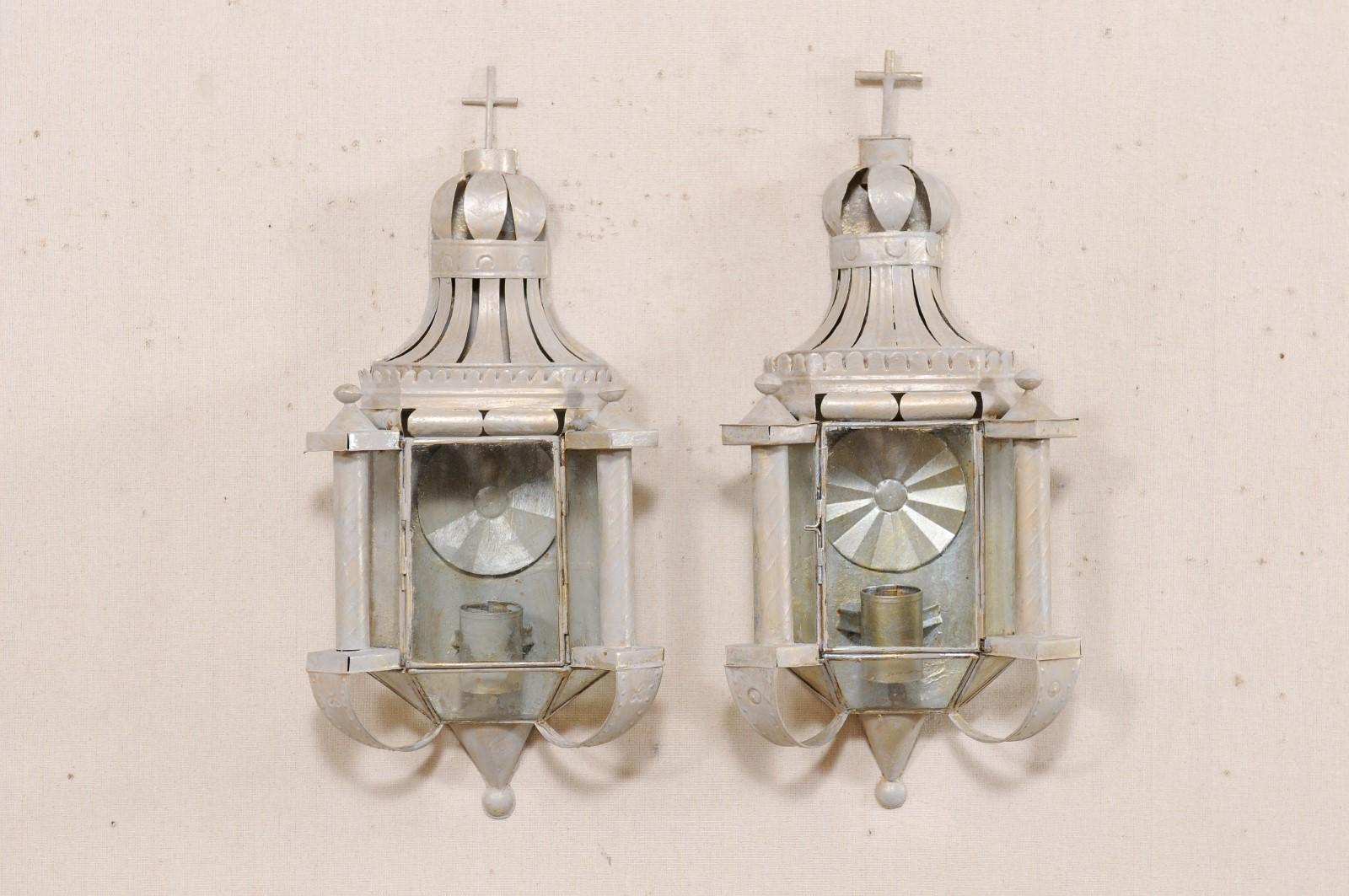 A pair of Mexican folk art sconces. This pair of whimsical single-candle sconces from Mexico have been hand-crafted from old tin, with a subtle gray paint wash over them. This pair of folk art sconces are lantern style and would look charming set