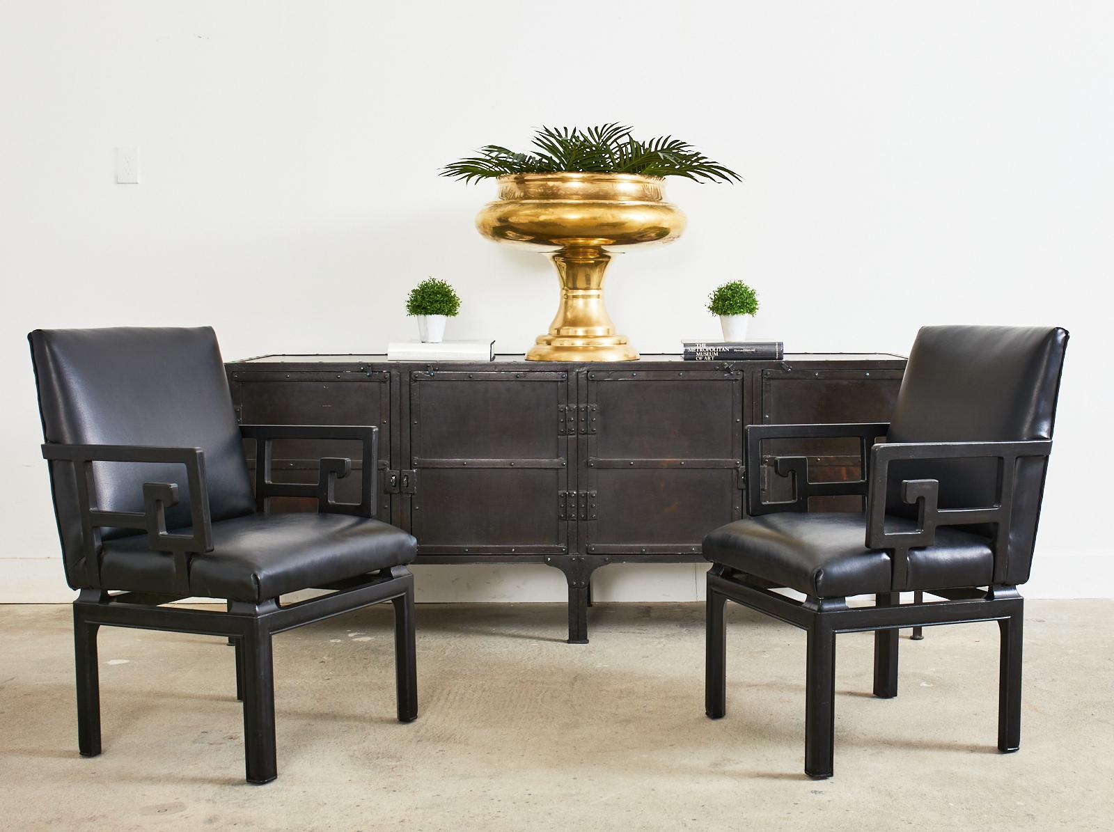 Rare Mid-Century Modern pair of Greek key armchairs designed by Michael Taylor for Baker Far East Collection. The chairs feature a hardwood frame with a black lacquered ebonized finish. The decorative arms have a large greek key motif. Generous