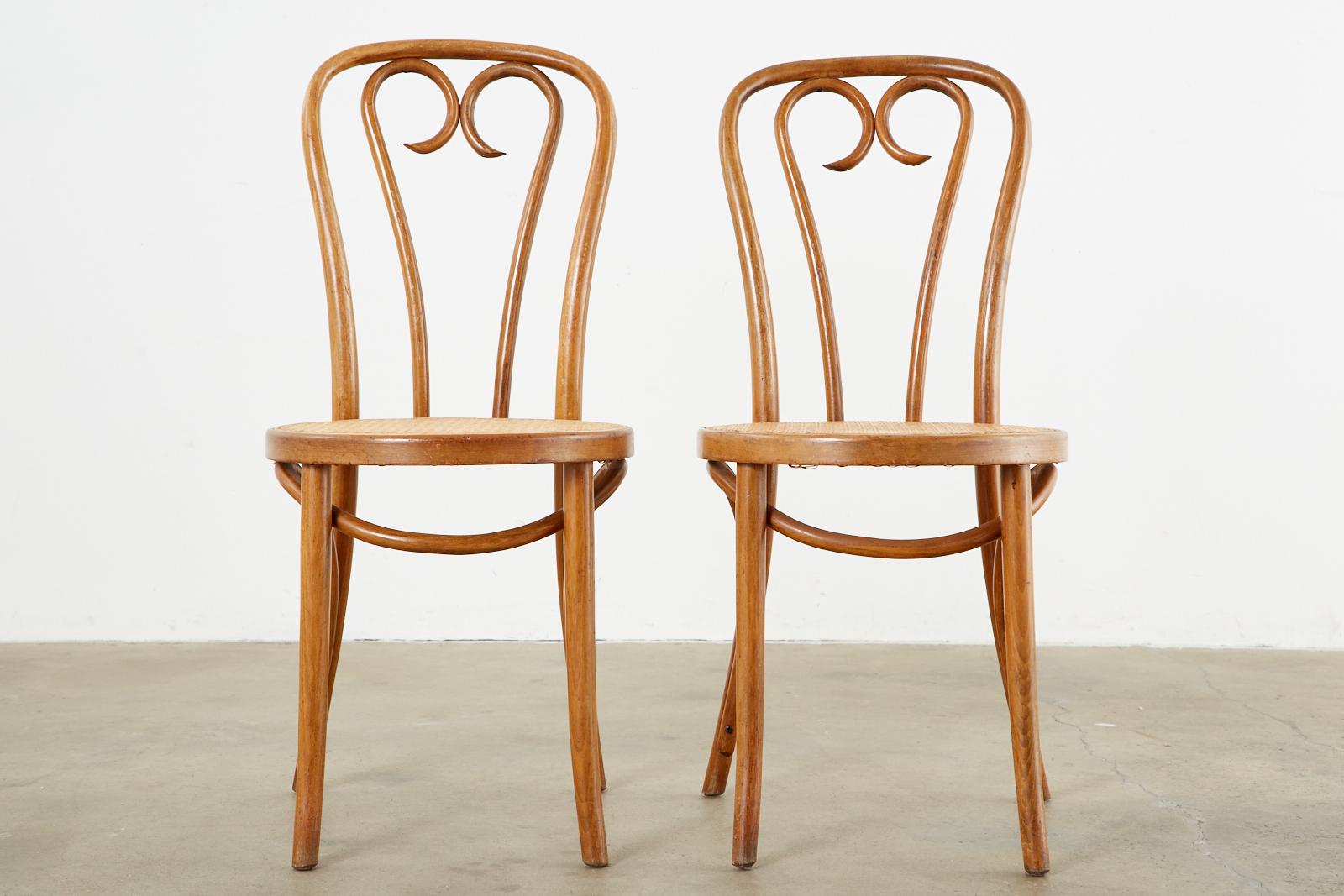 Matched pair of bentwood cafe bistro chairs designed by Michael Thonet know as the A-16 model. The chairs feature an iconic heart design back splat with a hand-caned seat. Beautifully crafted with a nicely aged patina on the finish. Original and