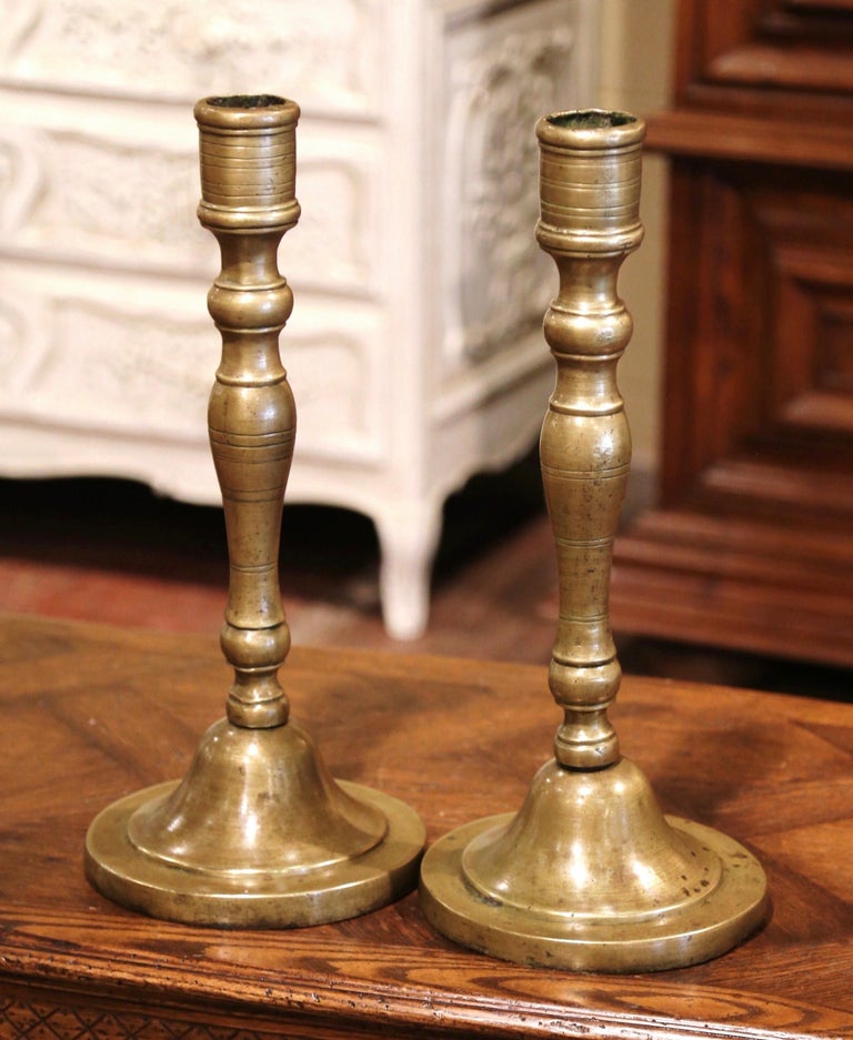 Decorate a mantel or a dining room table with this elegant pair of antique candlesticks; crafted in France circa 1750 and made of bronze, each candleholder stands on a round base over a turned stem. The heavy and tall candlesticks are in excellent