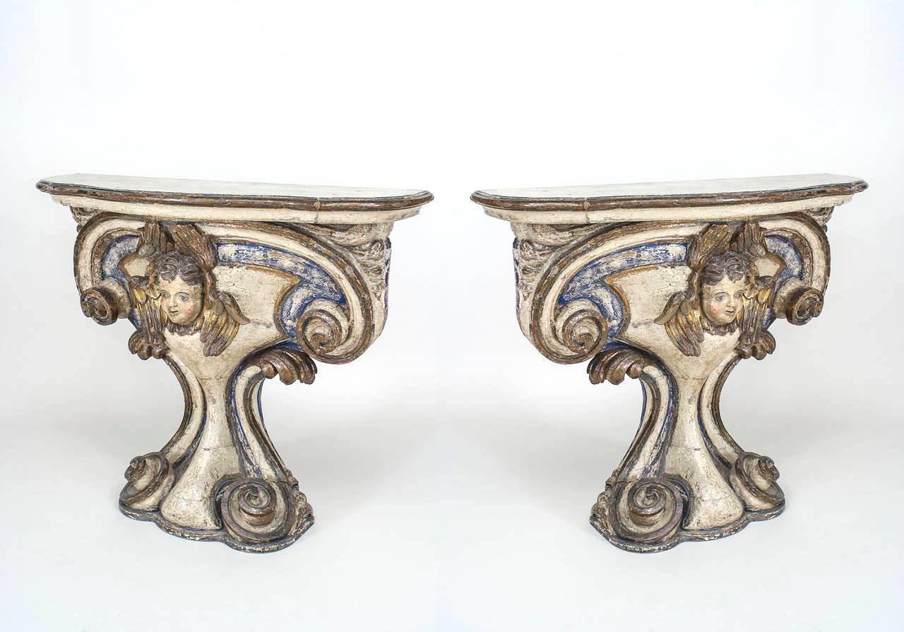Pair of Italian (mid-18th century) white painted & gilt trimmed pedestal base limewood console with carved scroll design sides and a centered cupid head with a faux marble top. (Priced as pair).
      