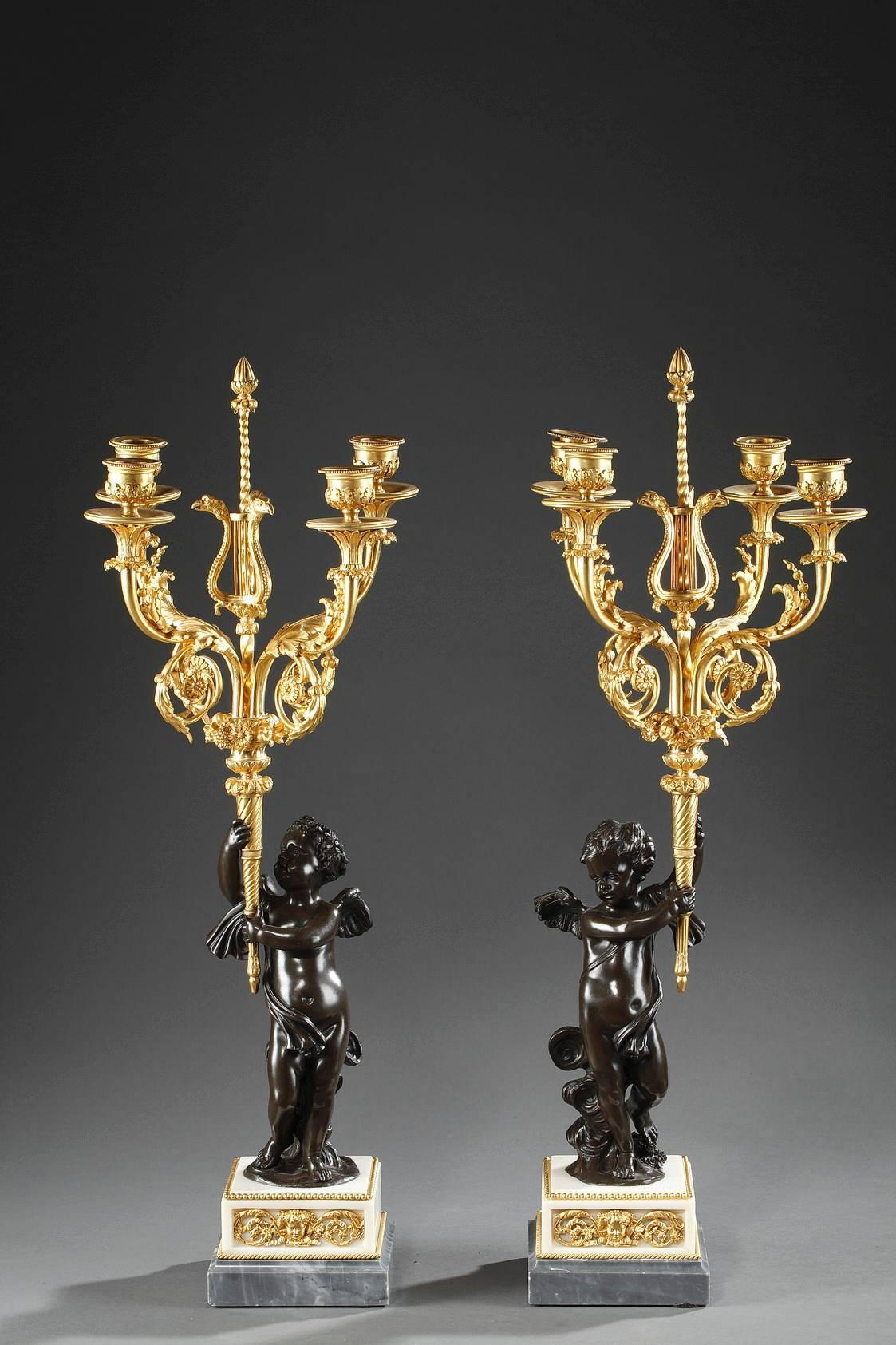 Exquisite pair of candelabra, composed of a young cupid on clouds in patinated bronze, holding an ormolu torch. A vase with flowers and fruits sits where the flame of the torch would be, and four candlestick arms extend out of the vase. The arms are