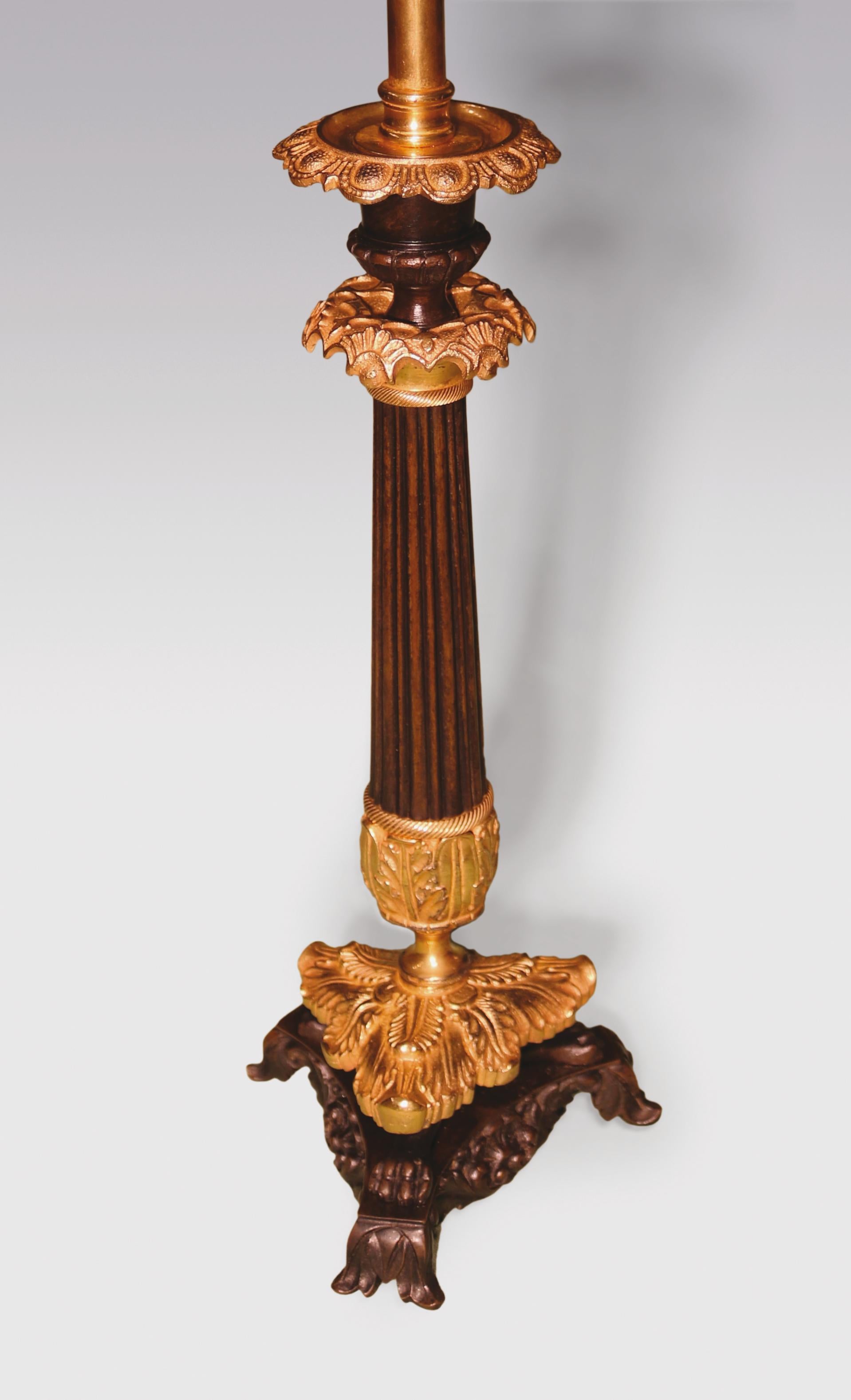 A pair of mid-19th century bronze and ormolu candlesticks, having petal shaped sconces above reeded tapering stems supported on acanthus decorated lion's paw triangular plinth bases ending on leaf scroll feet. (Now converted to lamps).