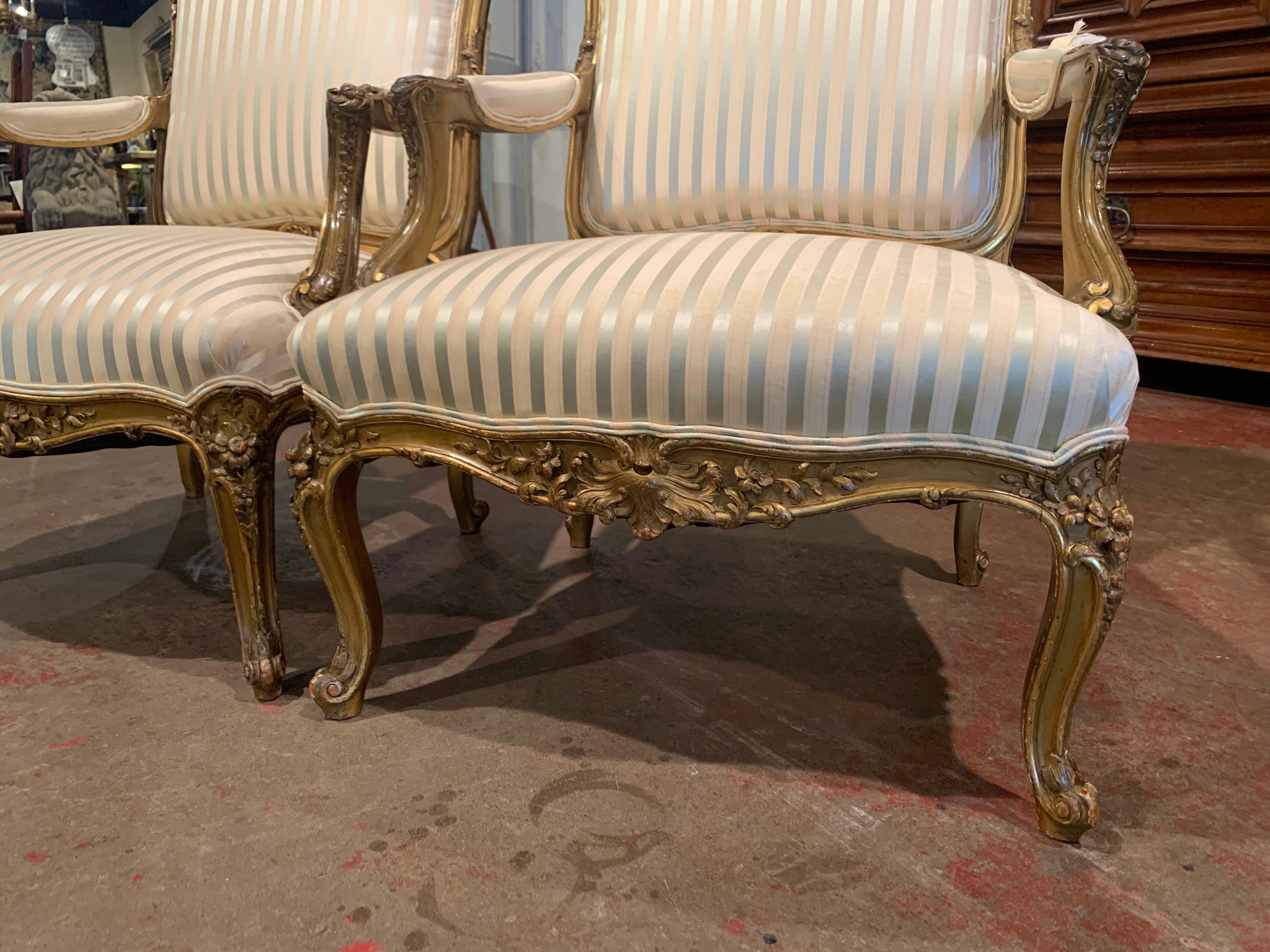 Crafted in France circa 1850, each antique armchair stands on cabriole legs decorated with floral and leaf motifs at the shoulder, and ending with escargot feet. The arched back covered with silk fabric is decorated with shell and foliage motifs,