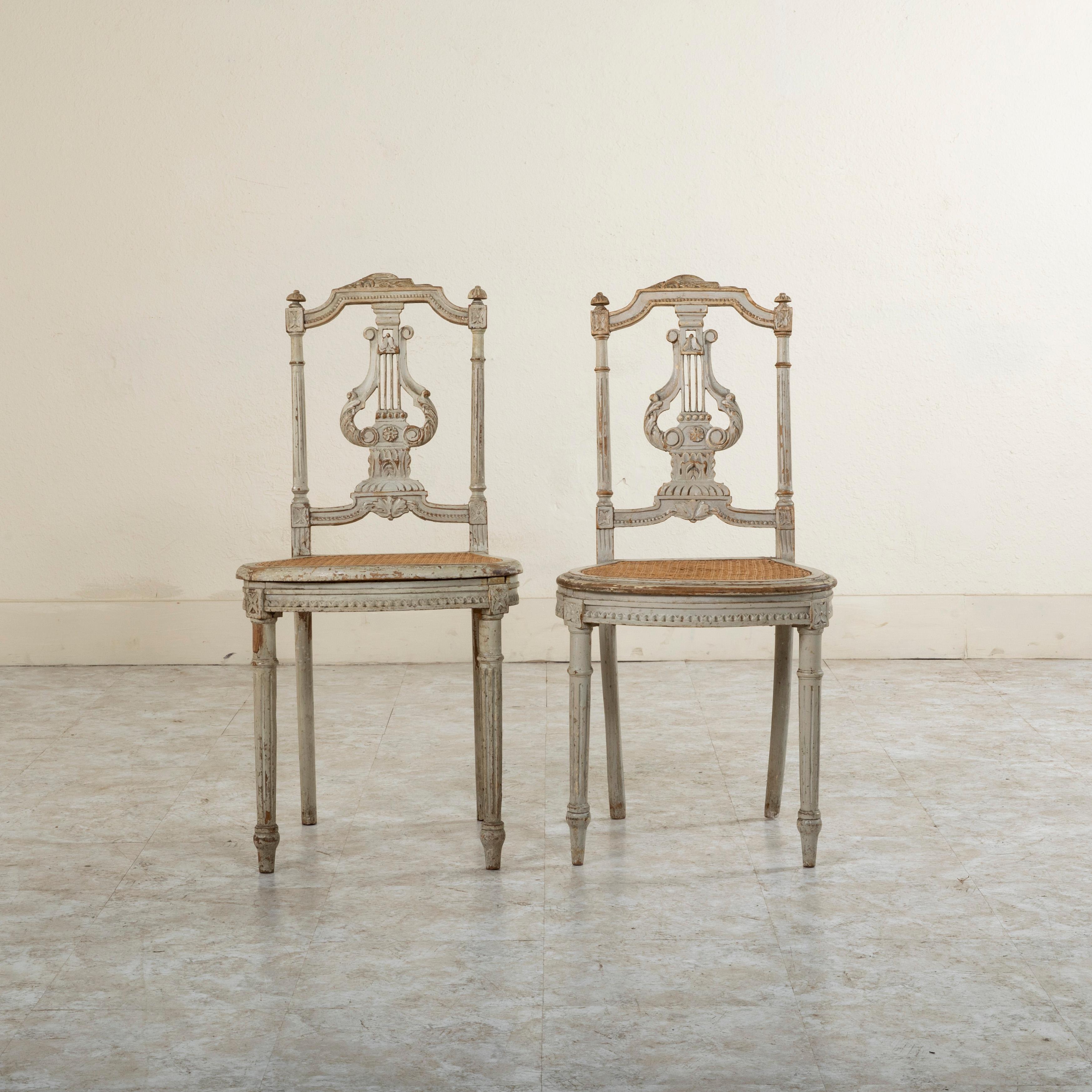 Cette paire de chaises d'opéra françaises de style Louis XVI du milieu du XIXe siècle présente des rosettes sculptées à la main au niveau des joints de matrice et une lyre centrale avec des feuilles en volutes dans le dossier de l'assise.... Le
