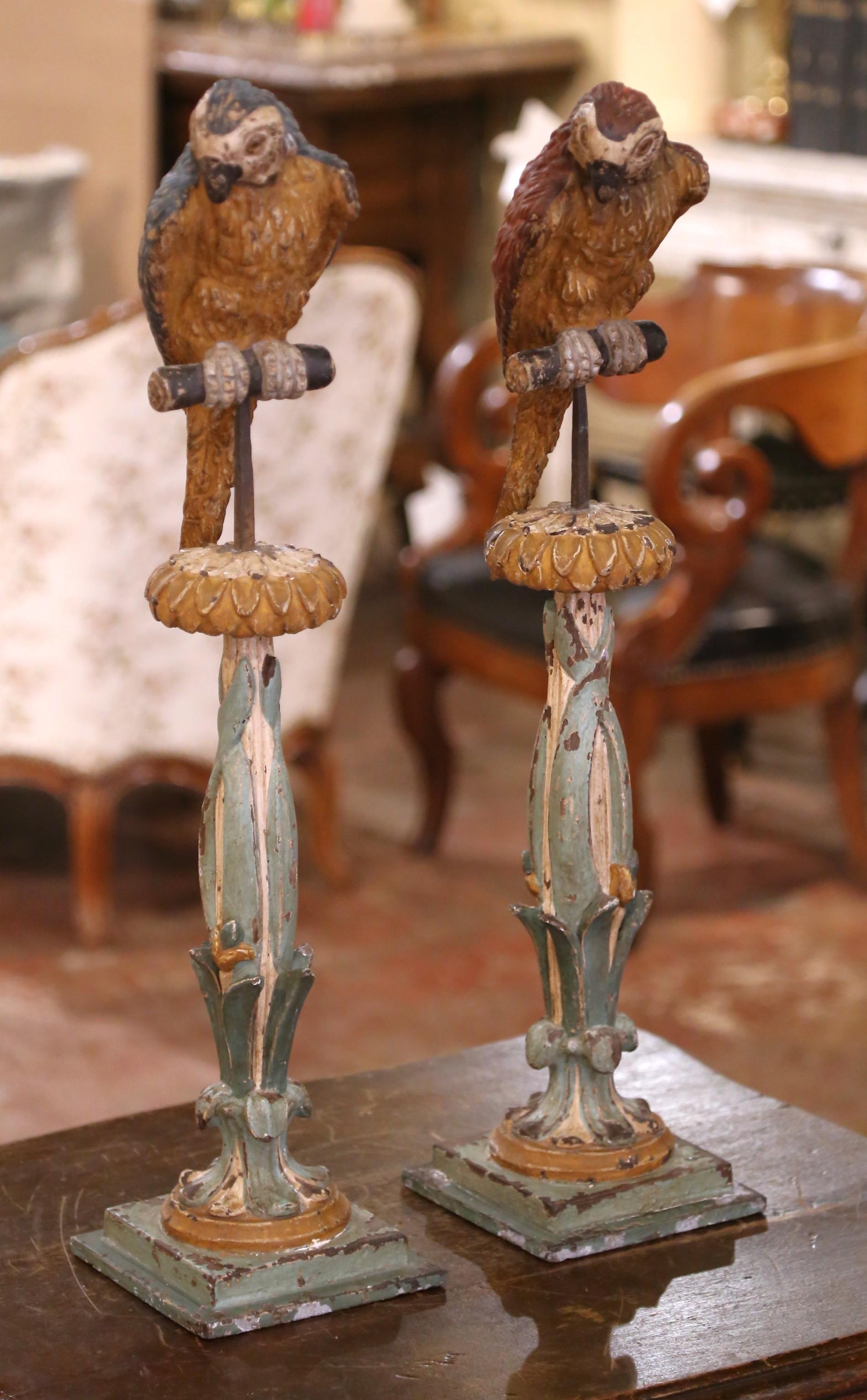 Whimsical and full of character, this rare pair of Italian carved wood candlestick stands was crafted circa 1850 and features finely detailed parrots perched in lively poses atop tall botanical columns. One bird is painted in rich red plumage, the