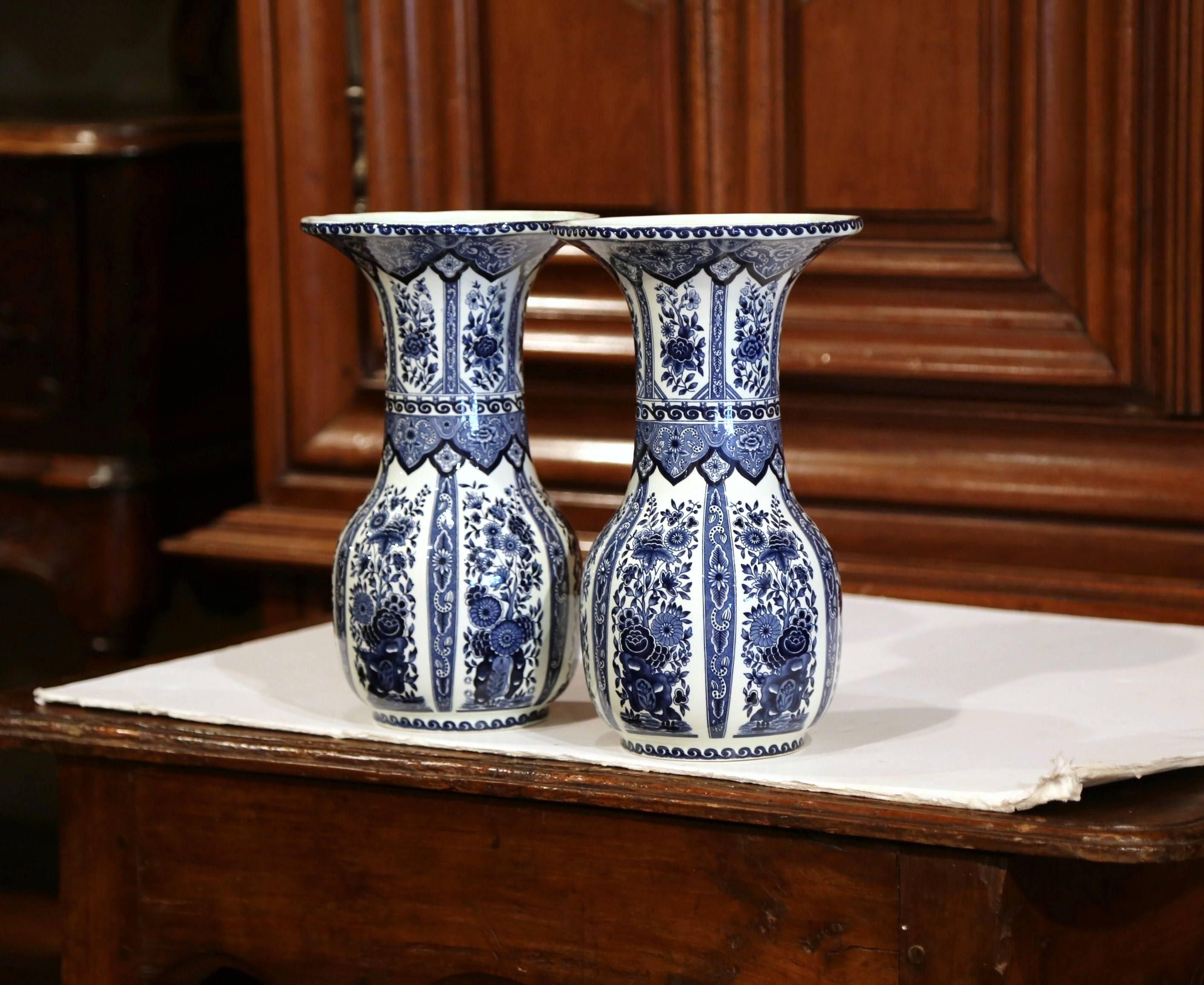 This vintage pair of ceramic Delft vases was created in Belgium, circa 1950. Round in shape, the ceramic flower vases feature traditional hand-painted floral decorations. They are stamped on the bottom, Bosh Belgium Delft. The porcelain pieces are