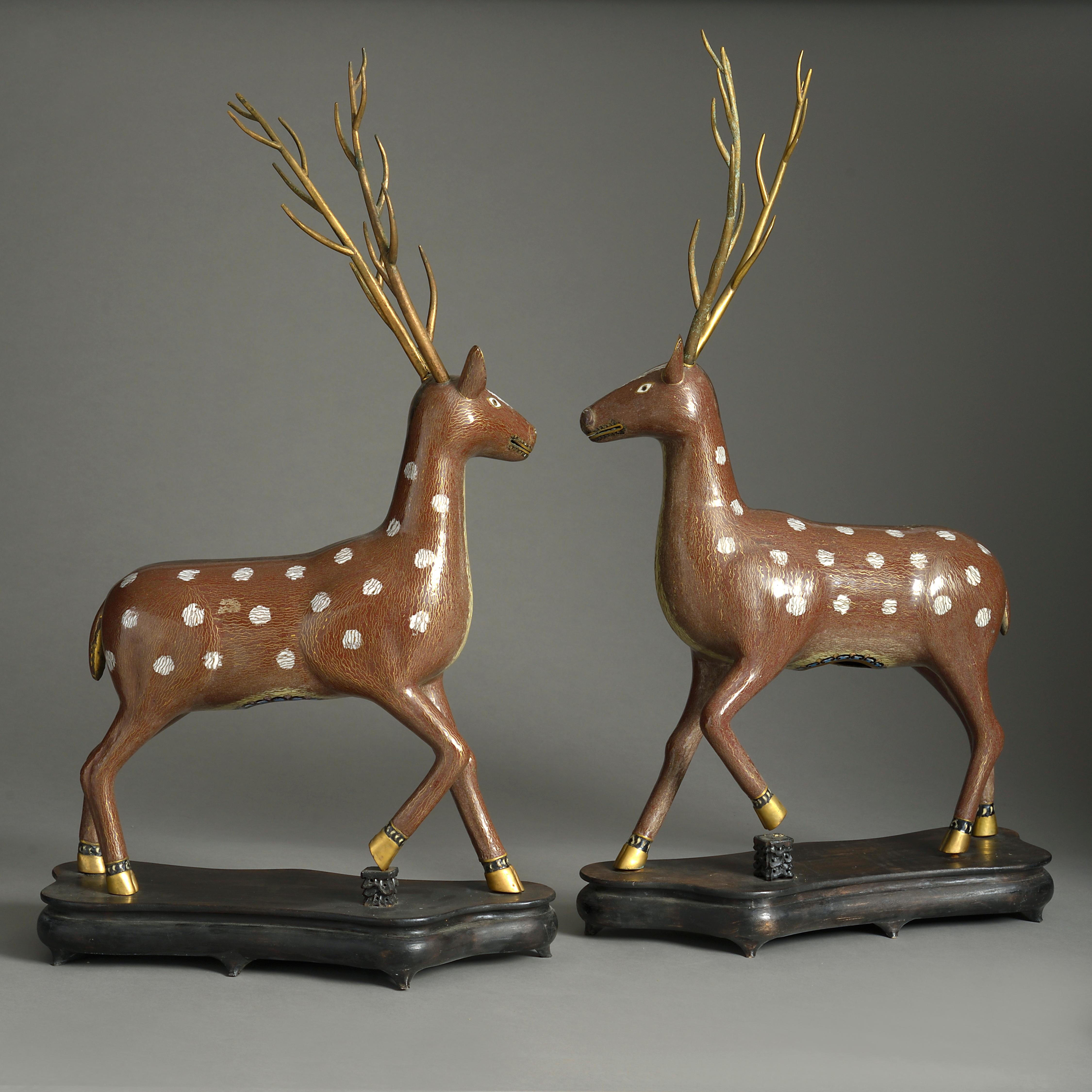 A pair of finely modelled mid-20th century cloisonné stags, having gilt metal antlers, the bodies with intricate enamel inlay, both set upon shaped ebonised wooden plinths.