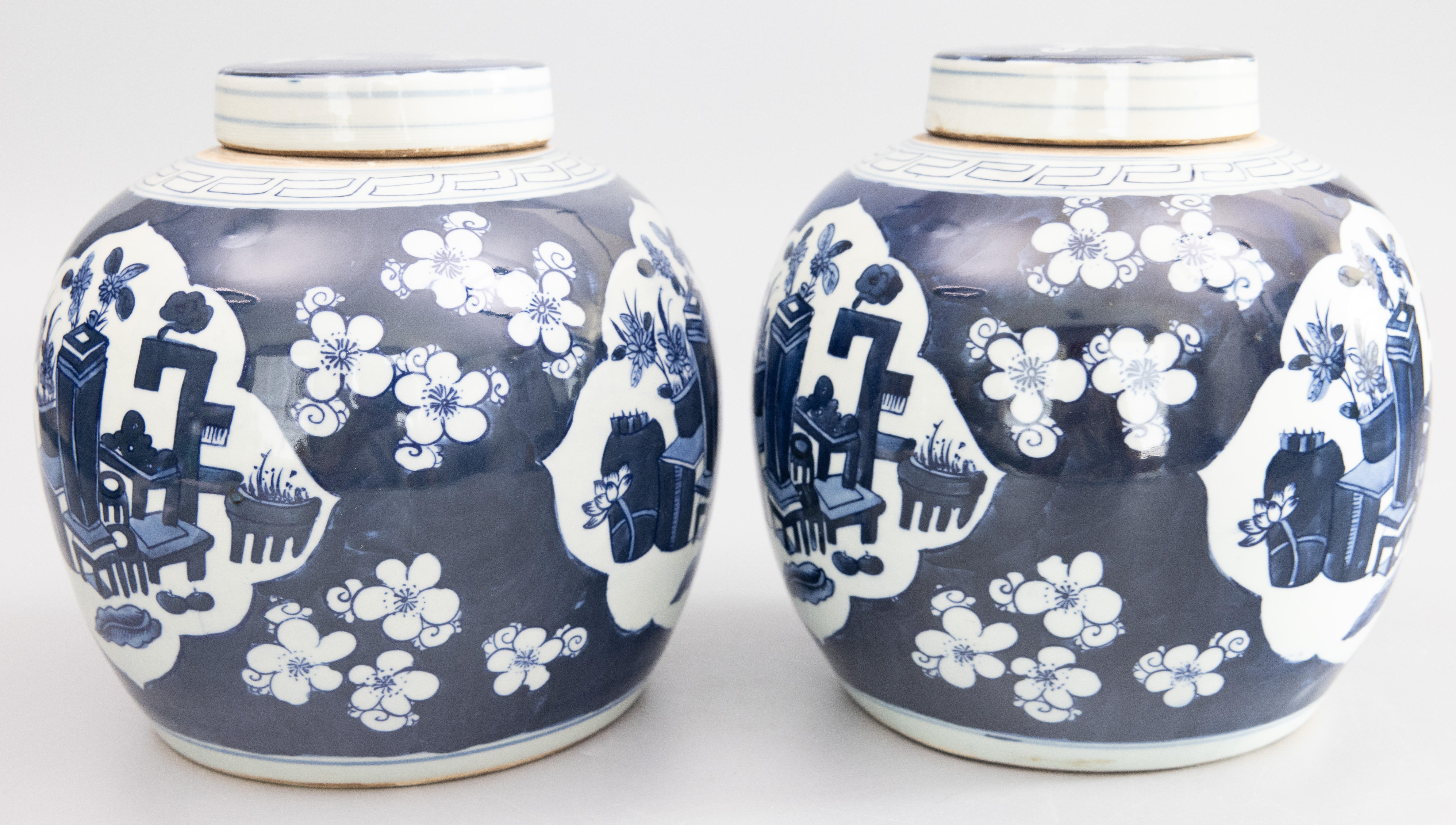 A lovely pair of vintage Chinese Kangxi style handmade ceramic lidded ginger jars hand painted in vibrant cobalt blue and white. These fabulous jars are decorated with flower pots in a patio scene surrounded by a cherry blossom floral motif.