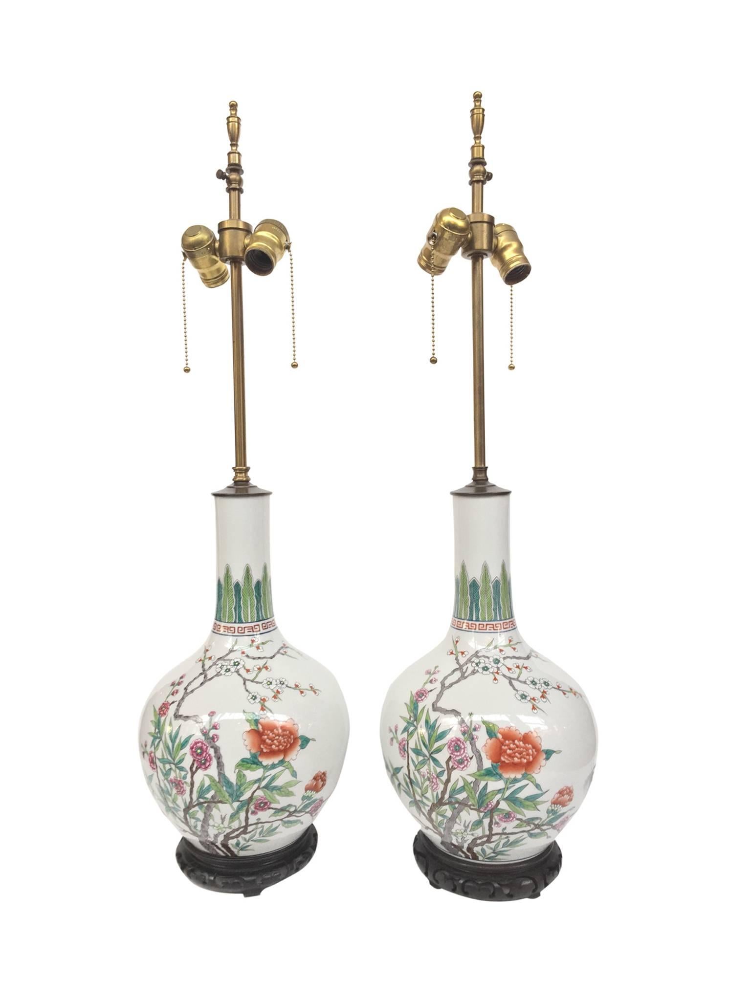 These white porcelain lamps are remarkable for their beautiful shape and design. Hand-painted floral motifs decorate the round body while a band of leaves encircle the long stem. The lamps are newly rewired with new brass hardware and new white