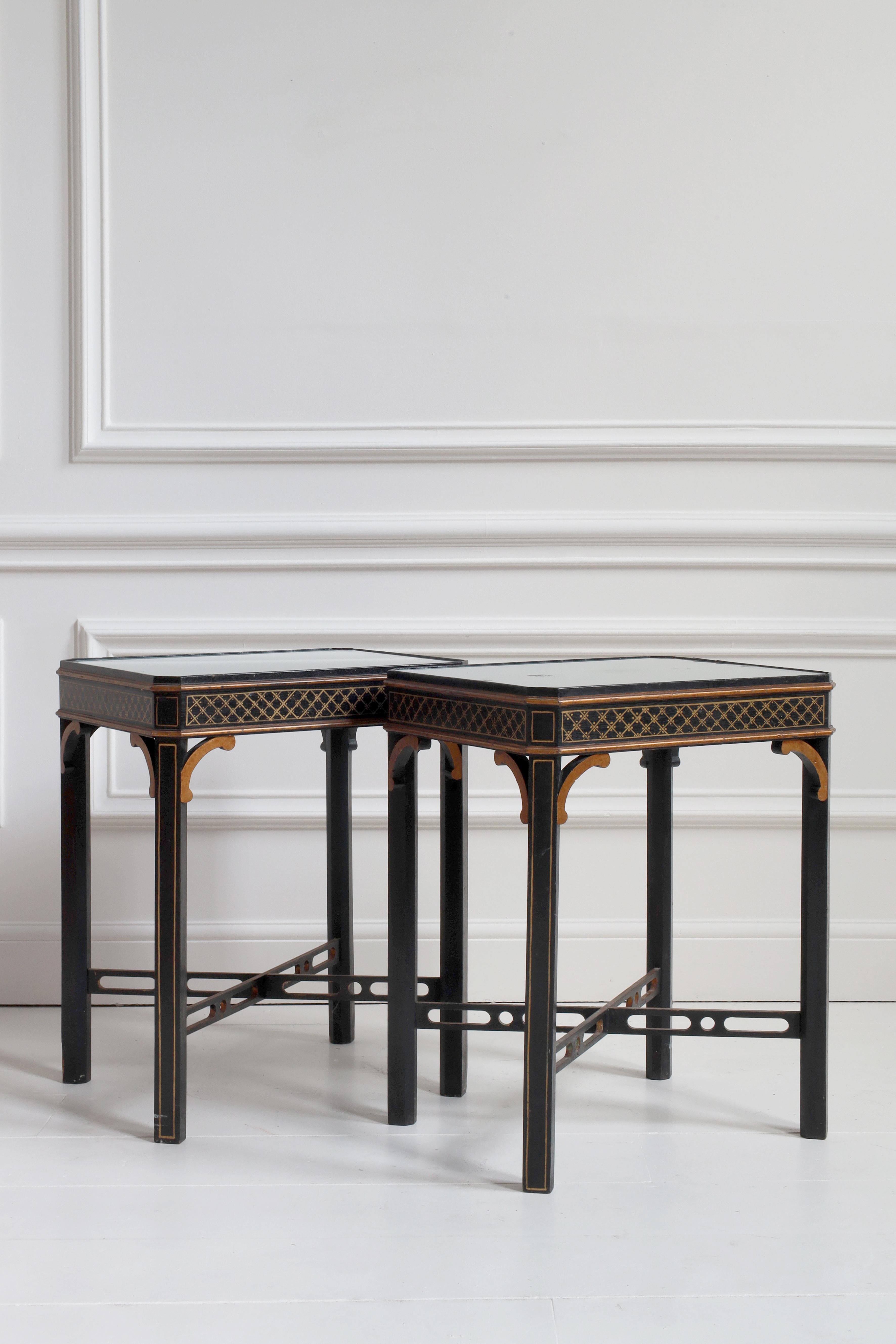 Un sofisticado par de mesas auxiliares de Chinoiserie de mediados del siglo XX, cada una con un motivo de celosía finamente pintado a mano en dorado sobre fondo lacado en negro. Los tableros cuadrados se elevan sobre elegantes patas unidas por