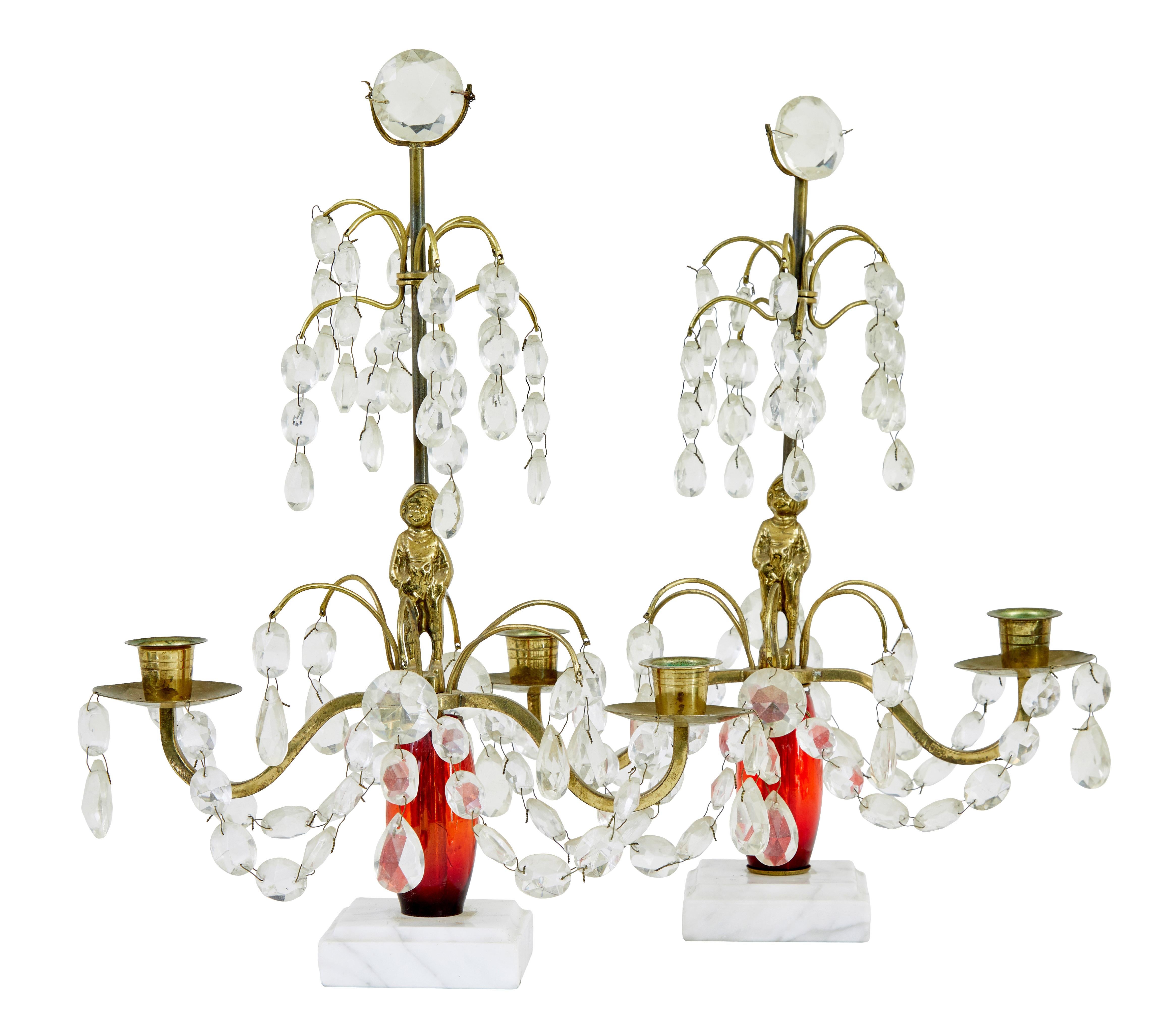 Pair of mid 20th century cut glass and marble candelabra circa 1960.

Main red plastic stem with a brass figure of boy in the centre.  2 brass arms with 2 candle fittings. Cut glass droplets, standing on a white marble base.

Minor dis-colouration